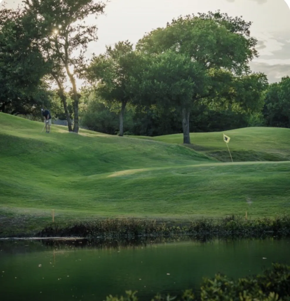 Golf course with mature trees, verdant green fairways, and a water feature