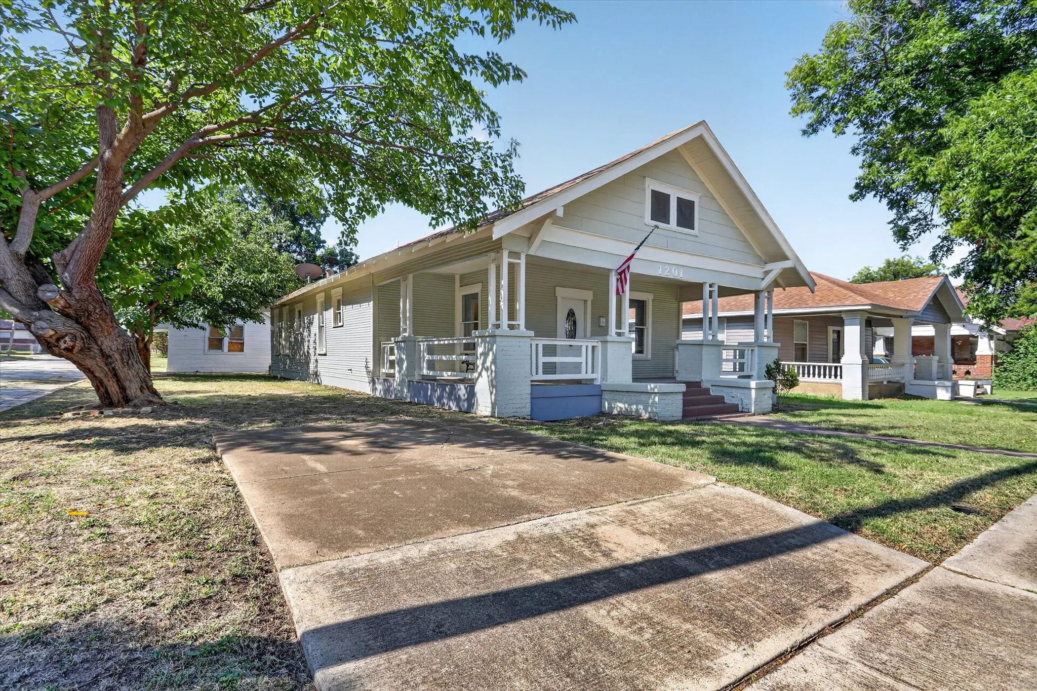 Light grey single-story home featuring a covered front porch with white columns, a gabled roofline, and visible house numbers