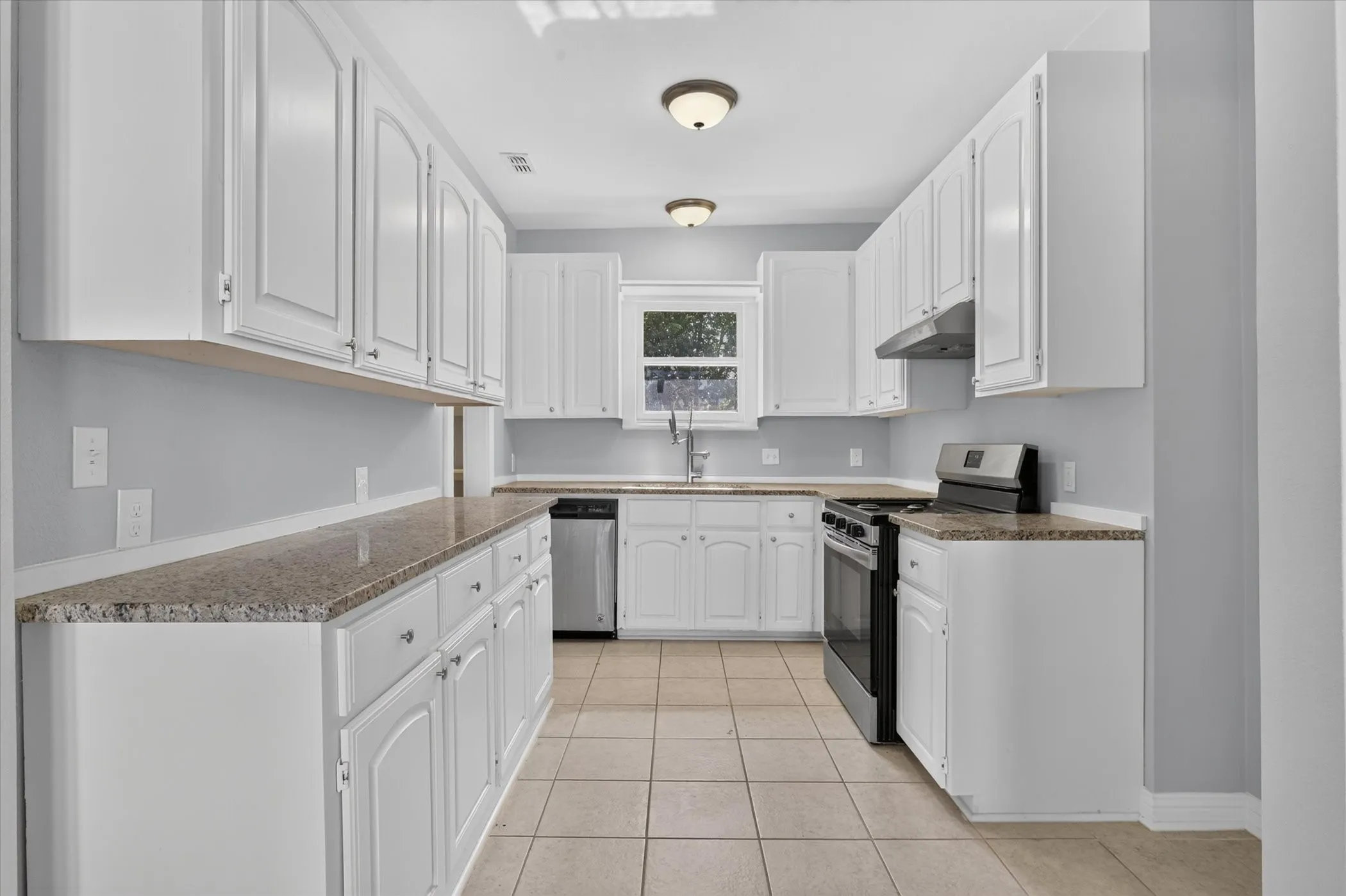 Kitchen featuring white cabinetry with silver hardware, speckled countertops, tile flooring, and stainless steel appliances