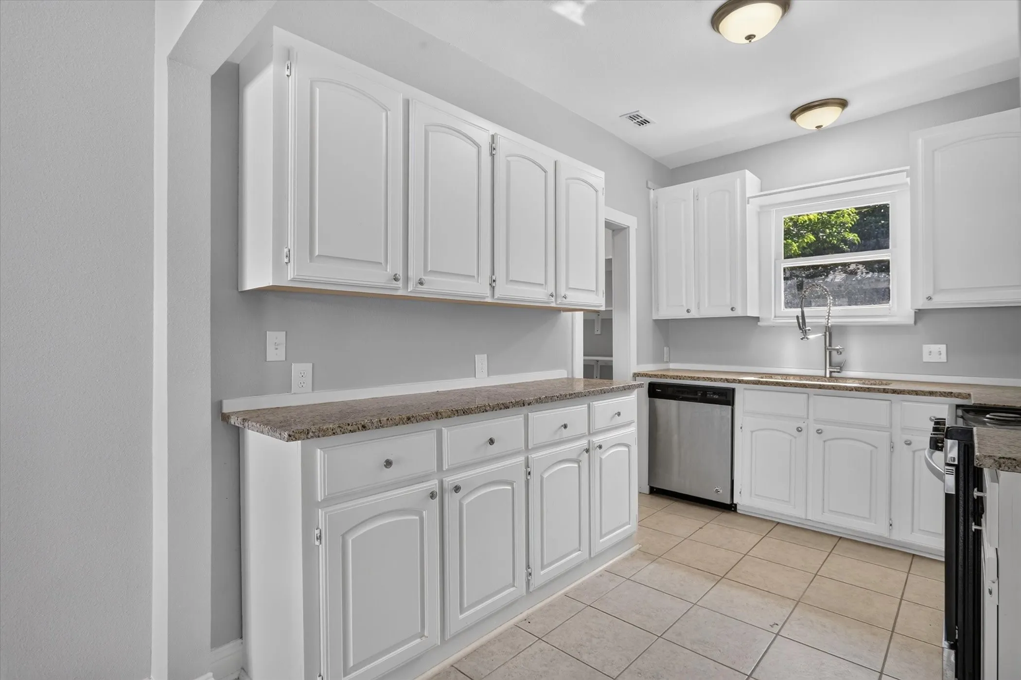 Kitchen featuring white cabinetry, speckled countertops, tile flooring, a stainless steel dishwasher, and a window with outdoor scenery