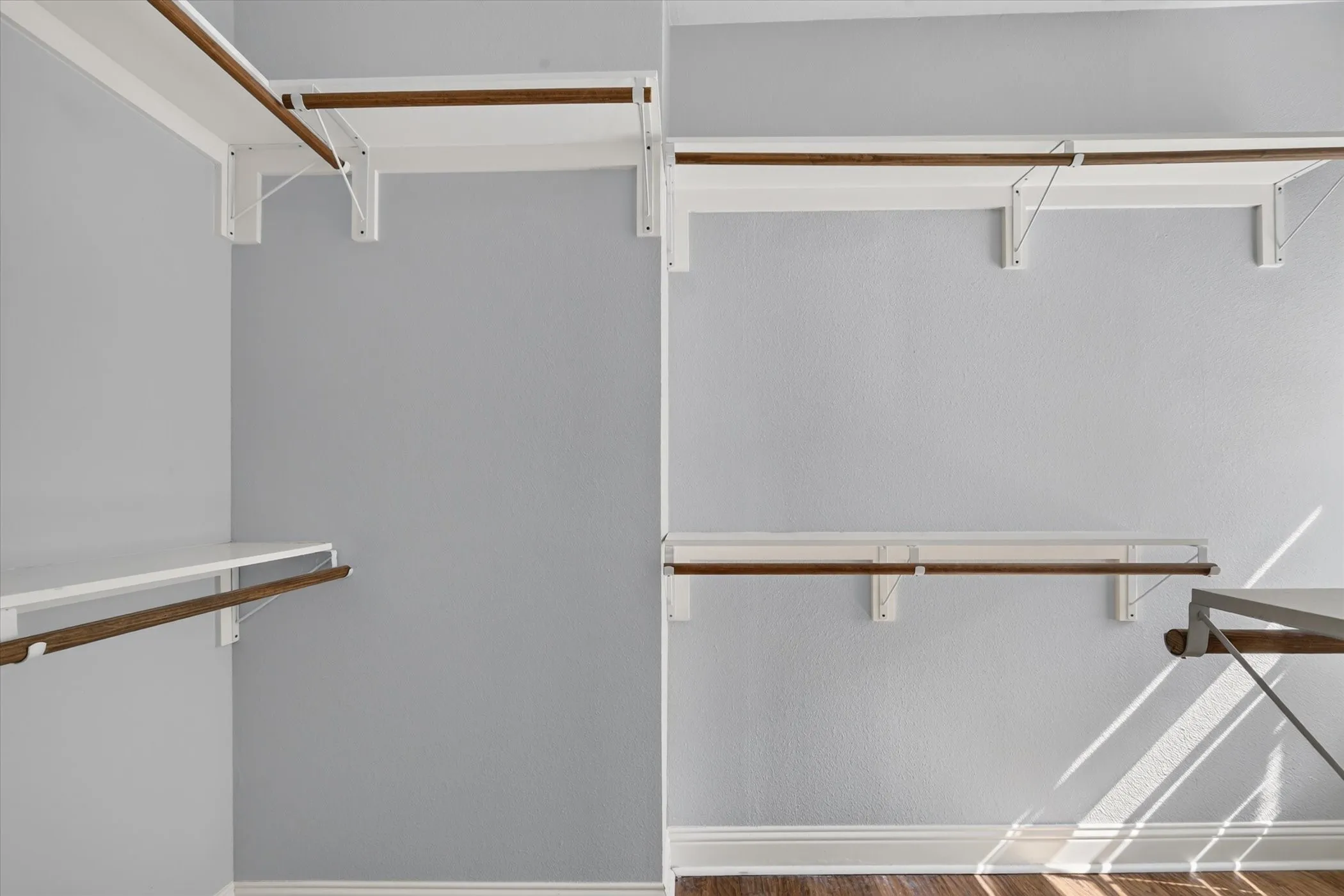Closet featuring built-in shelving and wood-finish hanging rods, light gray wall paint, white baseboards, and wood-finish flooring