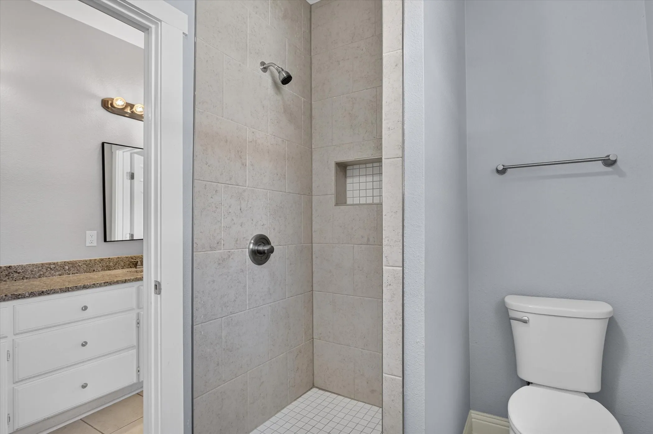Tiled shower stall featuring a built-in niche, white square mosaic tile floor, and brushed nickel fixtures