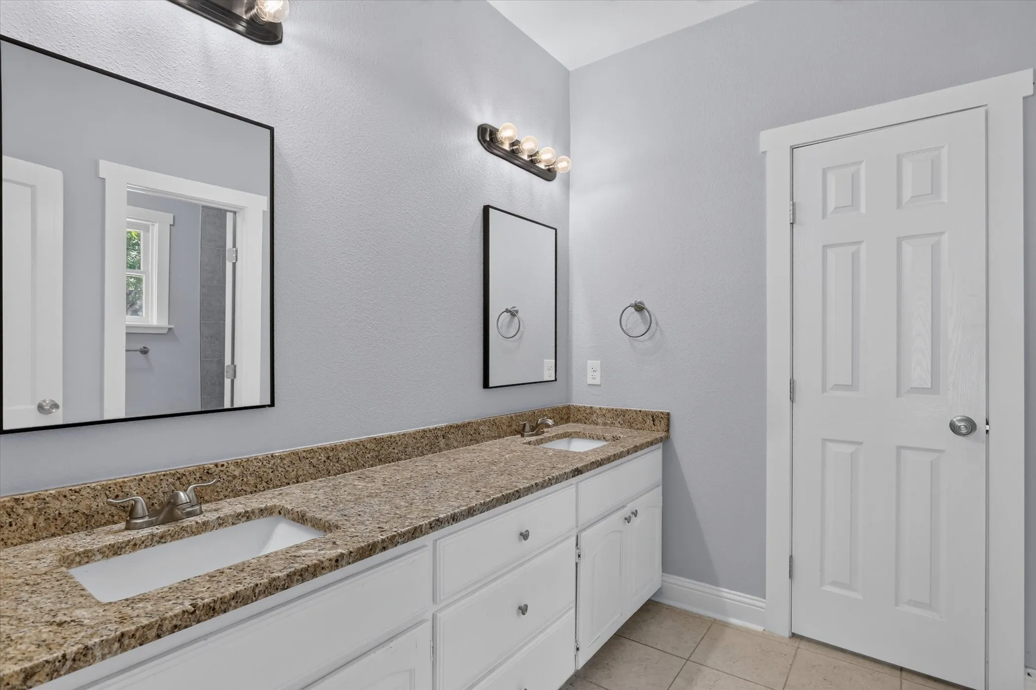 Spacious bathroom featuring a dual vanity with light-colored granite countertops, undermount sinks, and white cabinetry