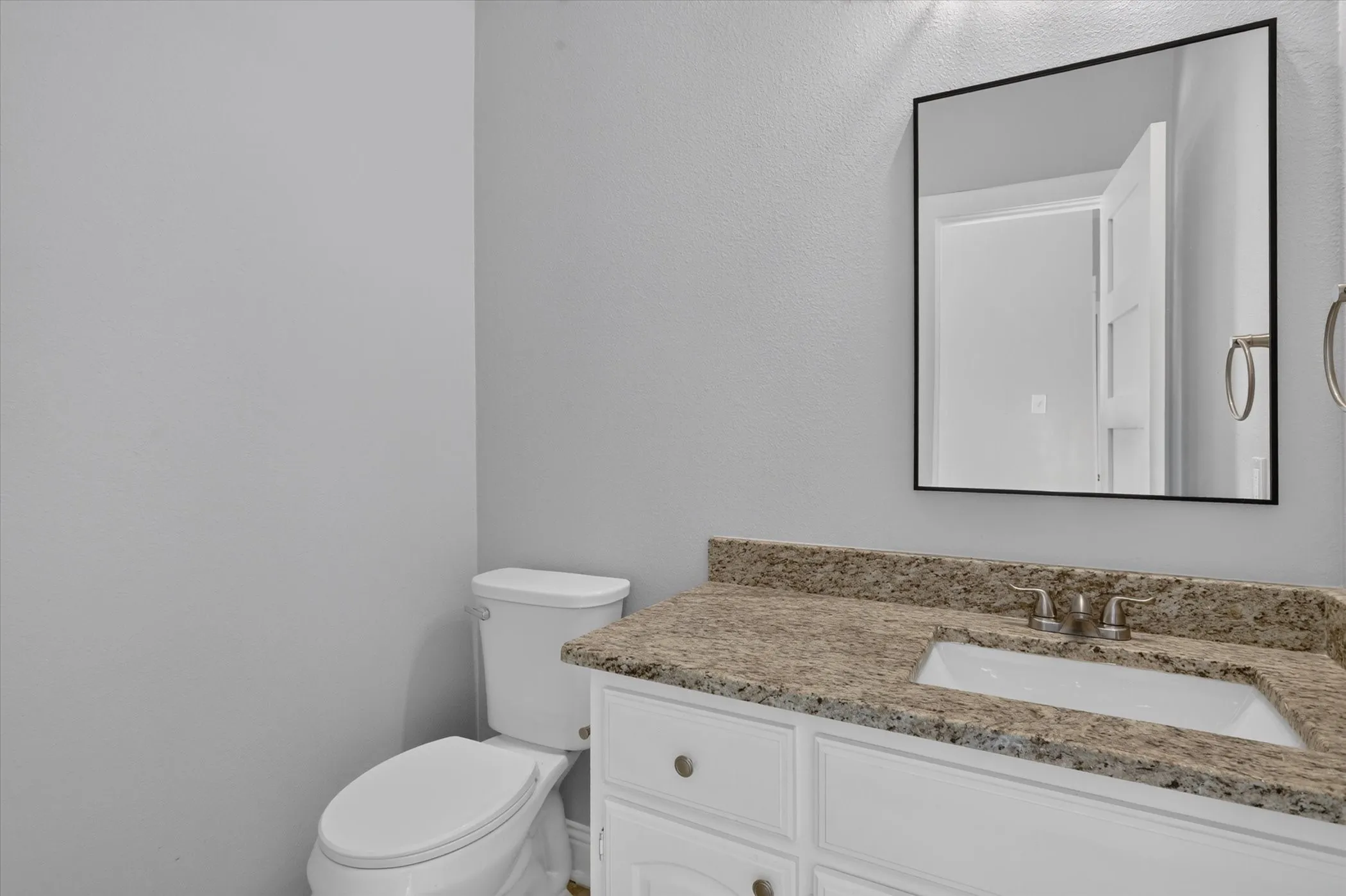 Bathroom vanity featuring a light-toned stone countertop, an undermount sink, and a framed mirror