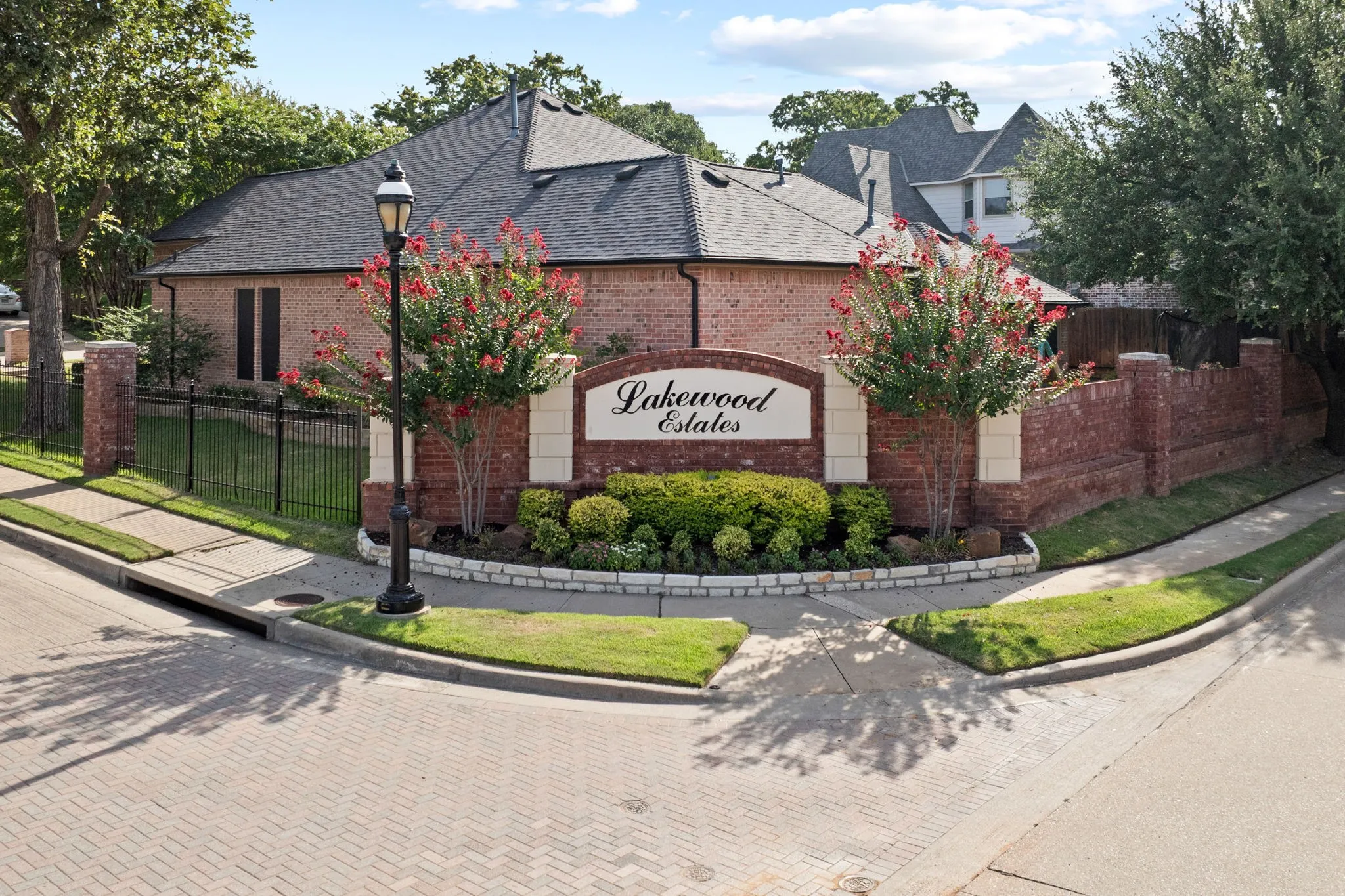 Brick entryway monument with "Lakewood Estates" signage, surrounded by mature landscaping and flowering trees