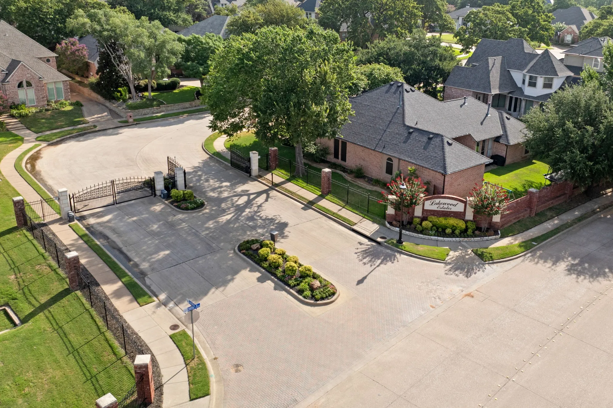 Gated community entrance featuring brick pillars, wrought iron fencing, and mature landscaping