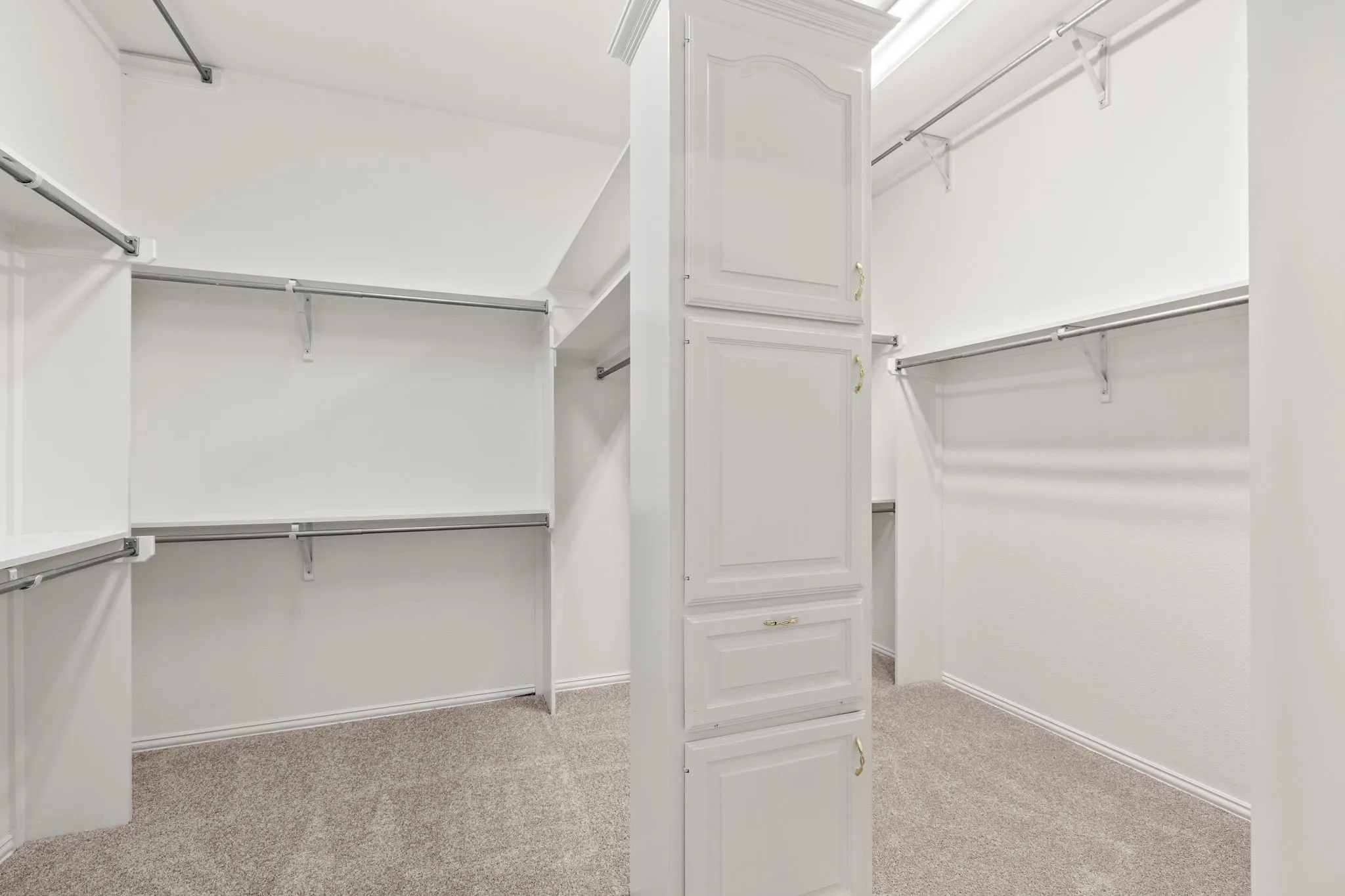 Spacious walk-in closet featuring built-in cabinetry, multiple hanging rods, shelving, and neutral carpeting
