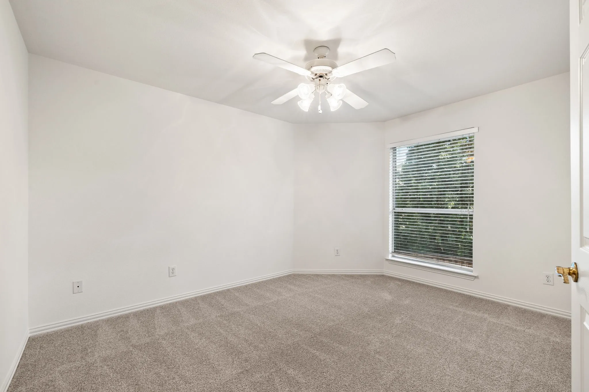 Spacious room featuring light gray carpet flooring, white walls, and a ceiling fan with light fixture