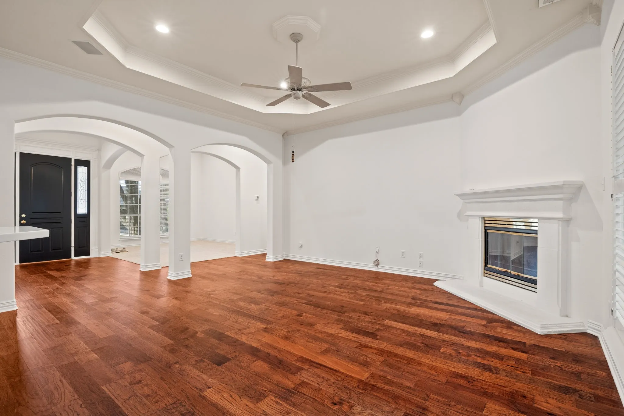 Living area featuring wood-finish flooring, a tray ceiling with recessed lighting, and a ceiling fan