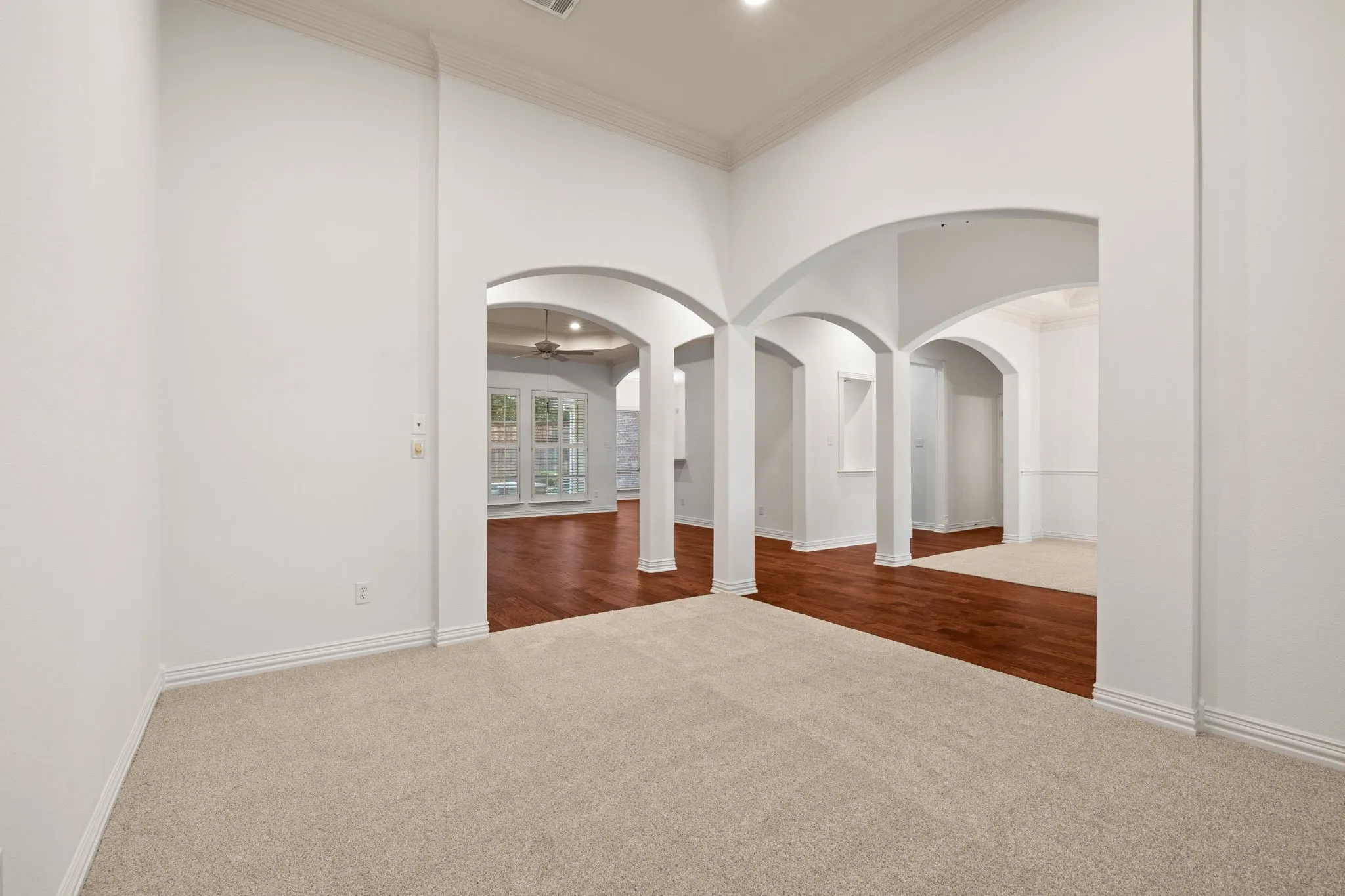 Interior space featuring arched doorways, light-toned carpeting, wood-finish flooring, white baseboards, and crown molding