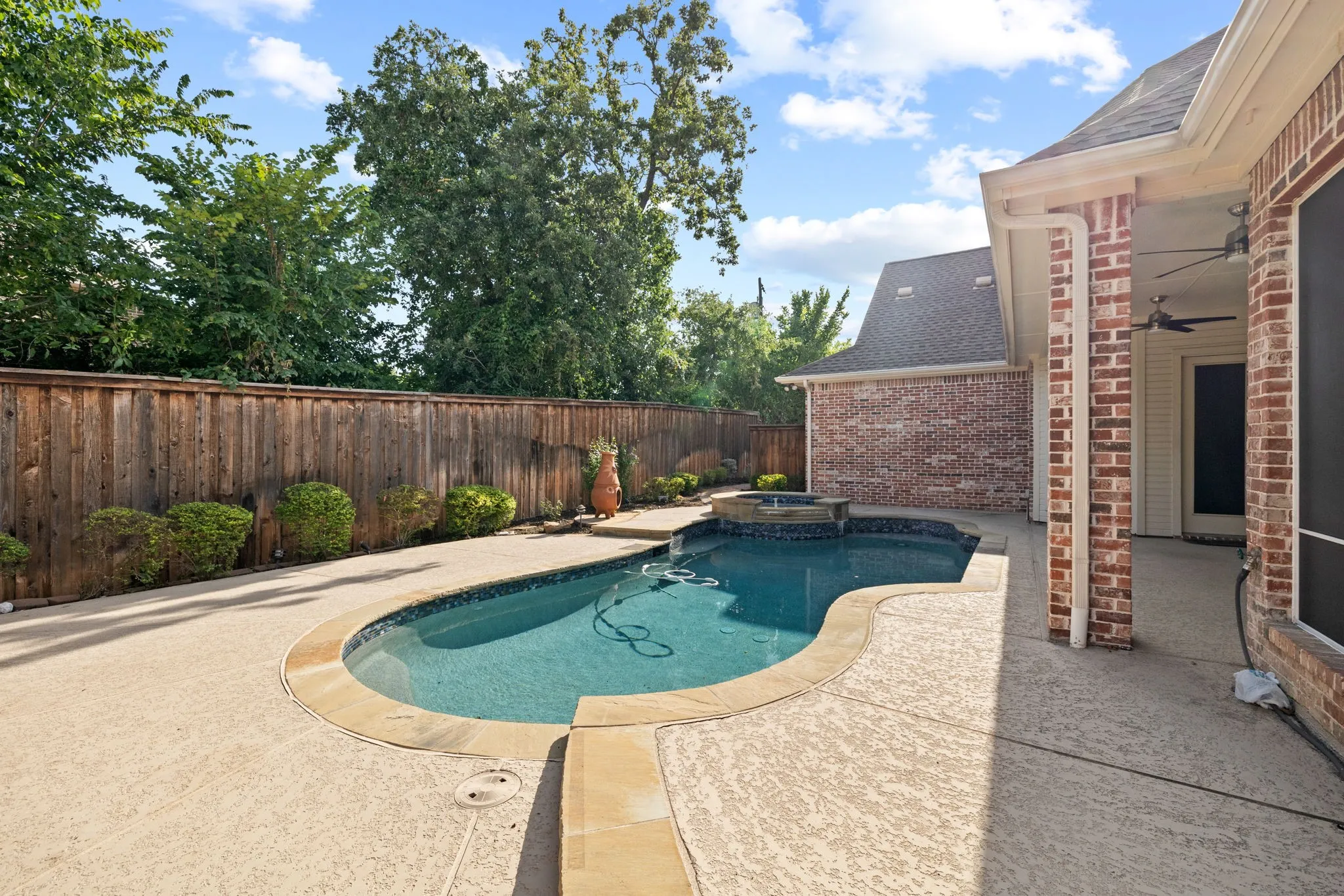 Curved swimming pool with an integrated spa, surrounded by textured concrete decking