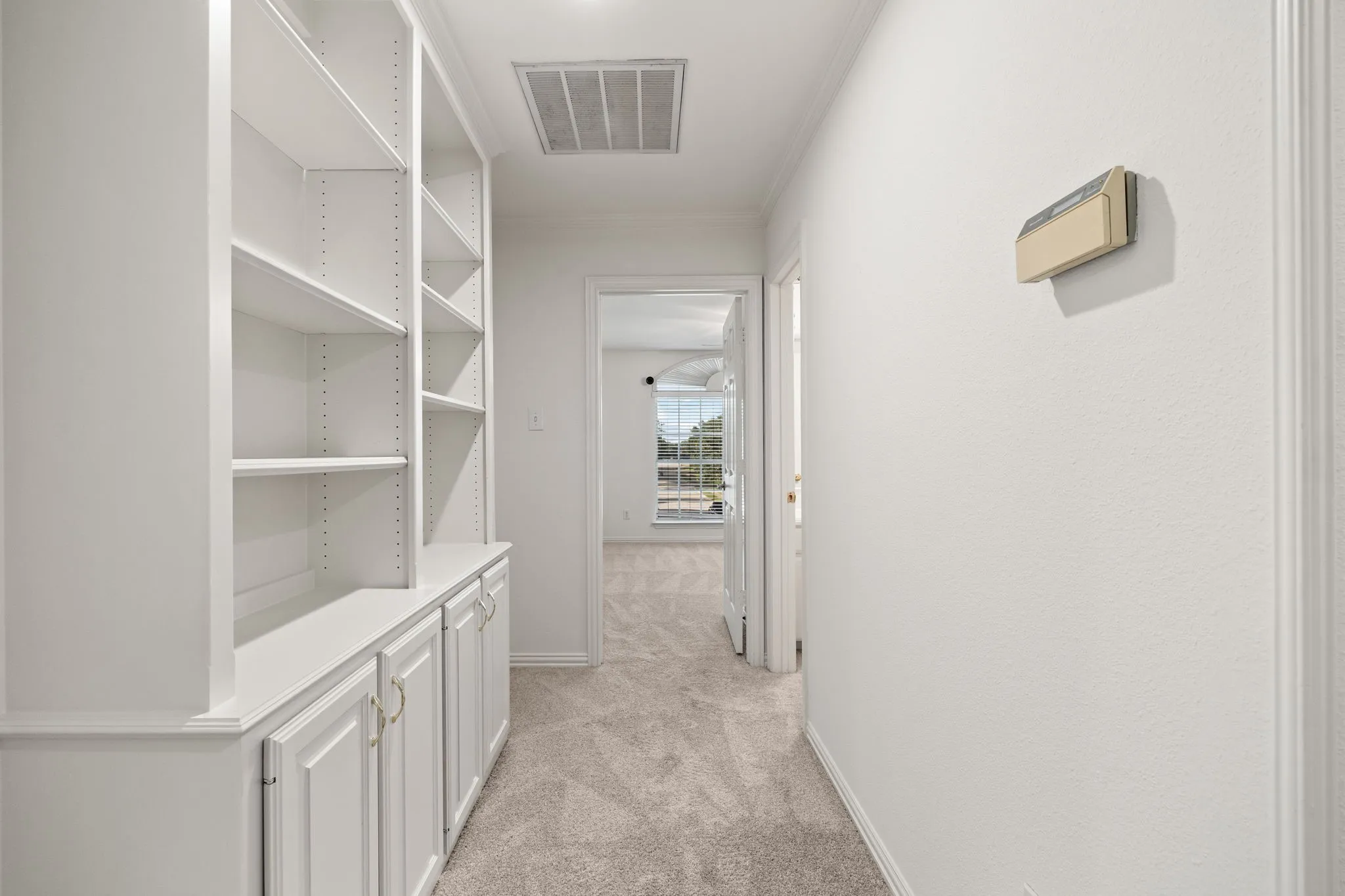 Hallway featuring built-in white cabinetry with adjustable shelving, recessed lighting, and neutral carpet flooring