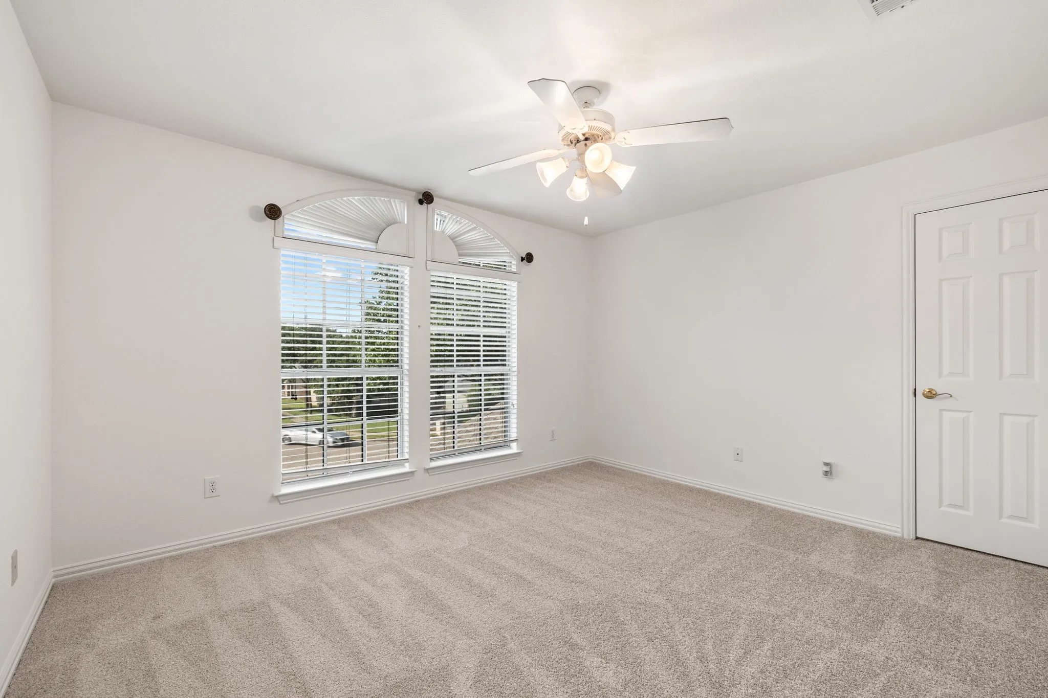 Bright room featuring arched windows, neutral carpet, white walls, and a ceiling fan