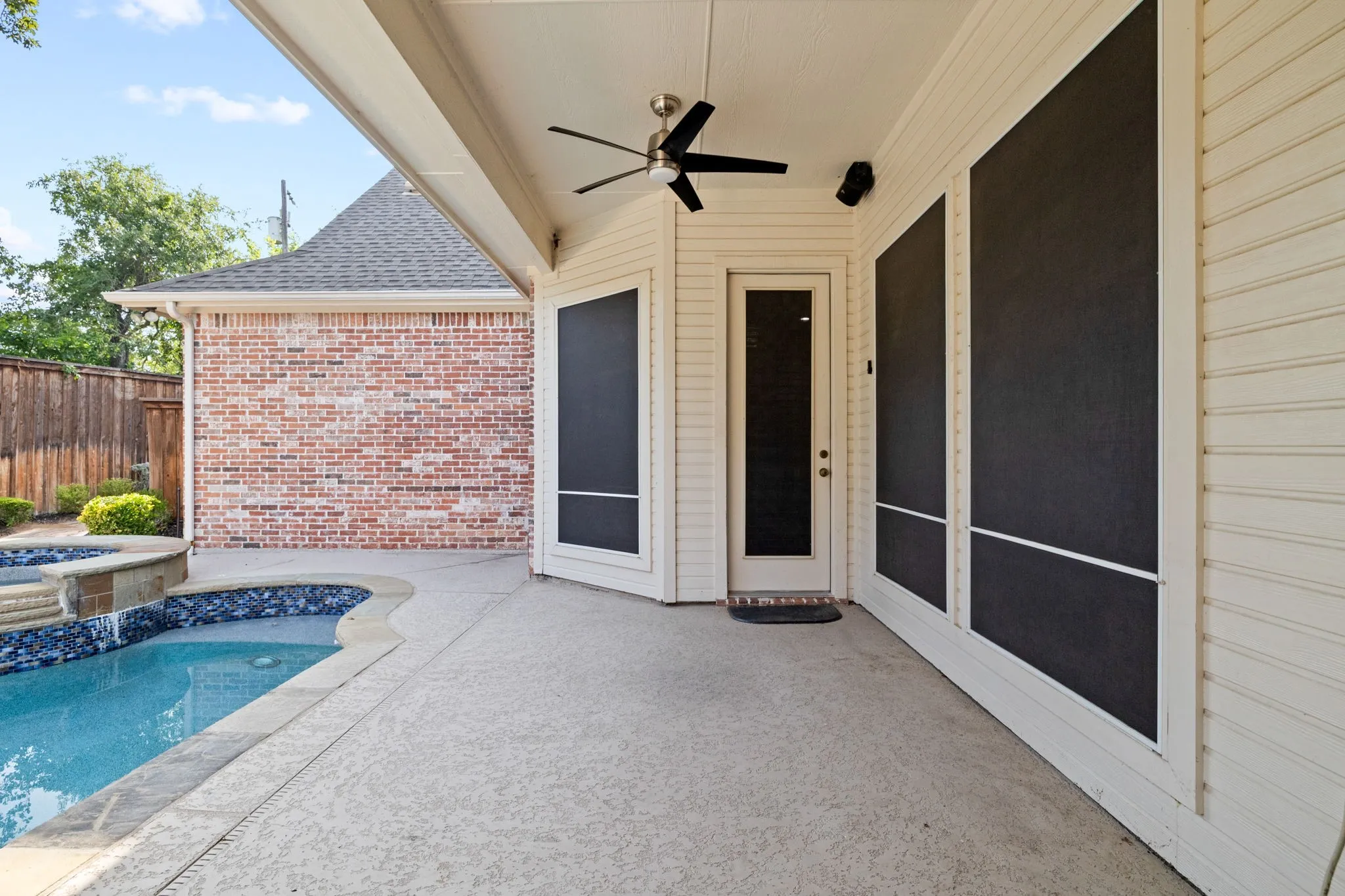 Covered patio with a ceiling fan, light-colored concrete flooring, and a door with a full-length glass panel