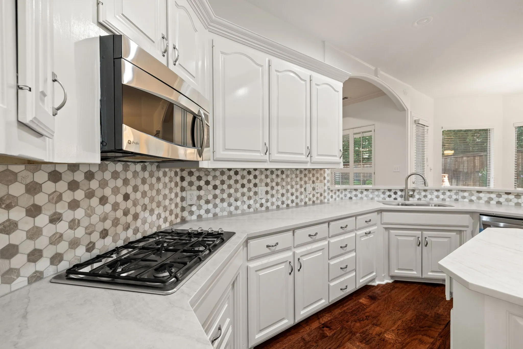 Contemporary kitchen featuring white cabinetry, a hexagonal tile backsplash, stainless steel appliances, and a gas cooktop