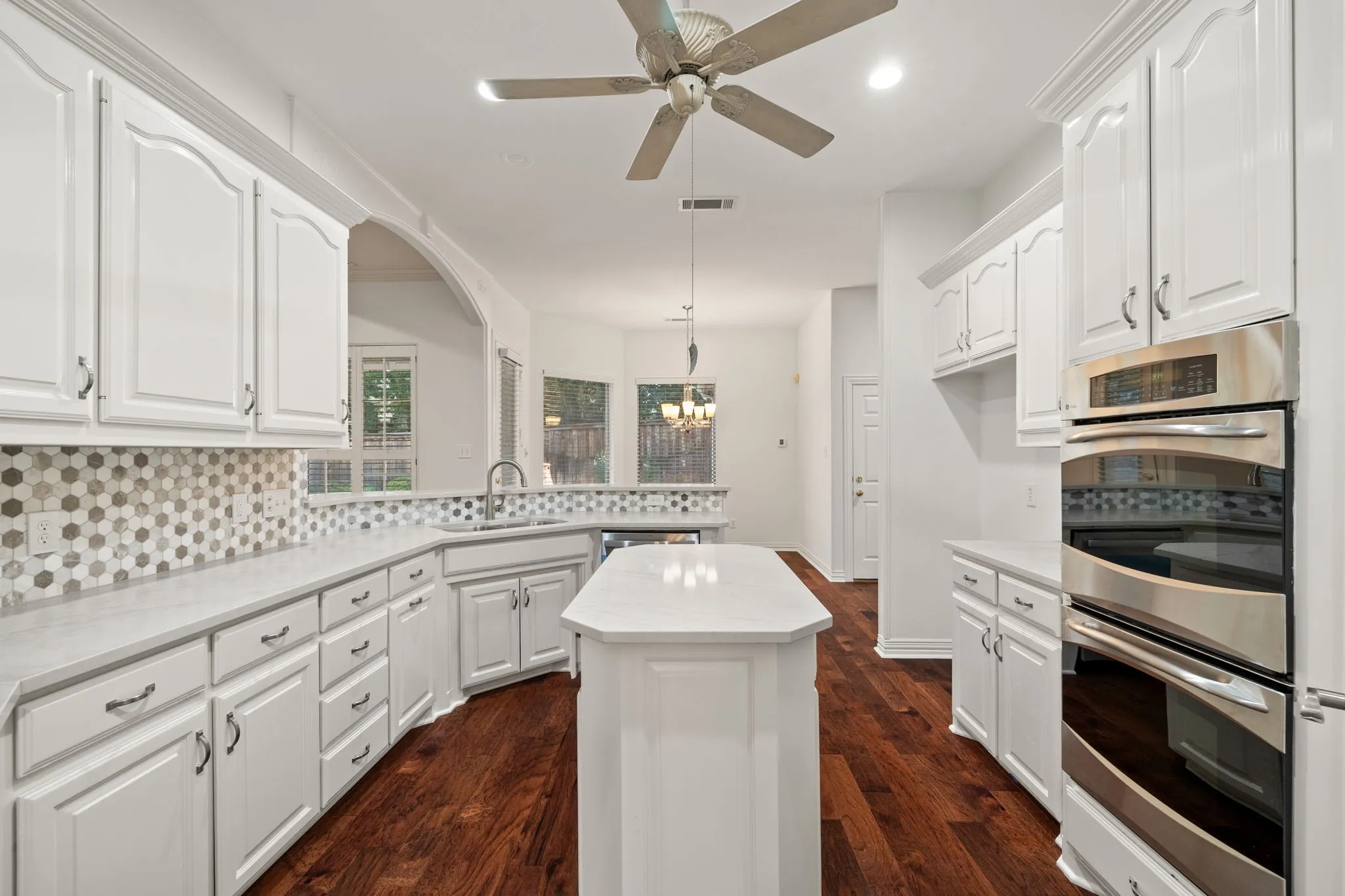 Bright kitchen featuring white cabinetry, light countertops, a mosaic tile backsplash, wood-finish flooring, and stainless steel double ovens