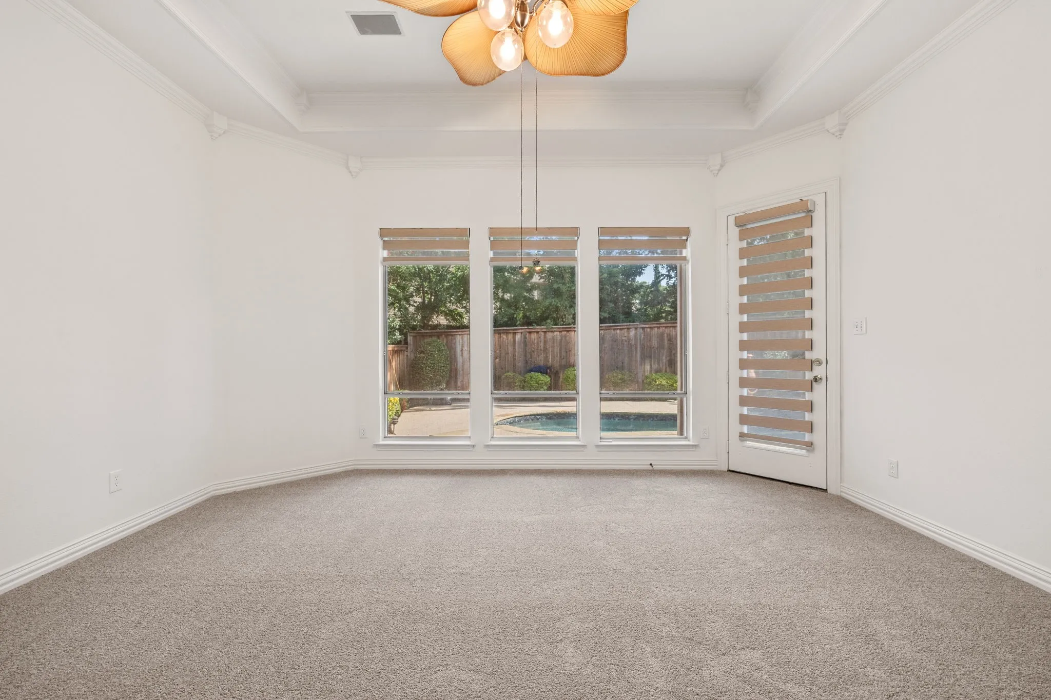 Room featuring a large three-panel window overlooking a pool, a glass-paneled door, recessed ceiling, crown molding, and a decorative ceiling fan with light fixture