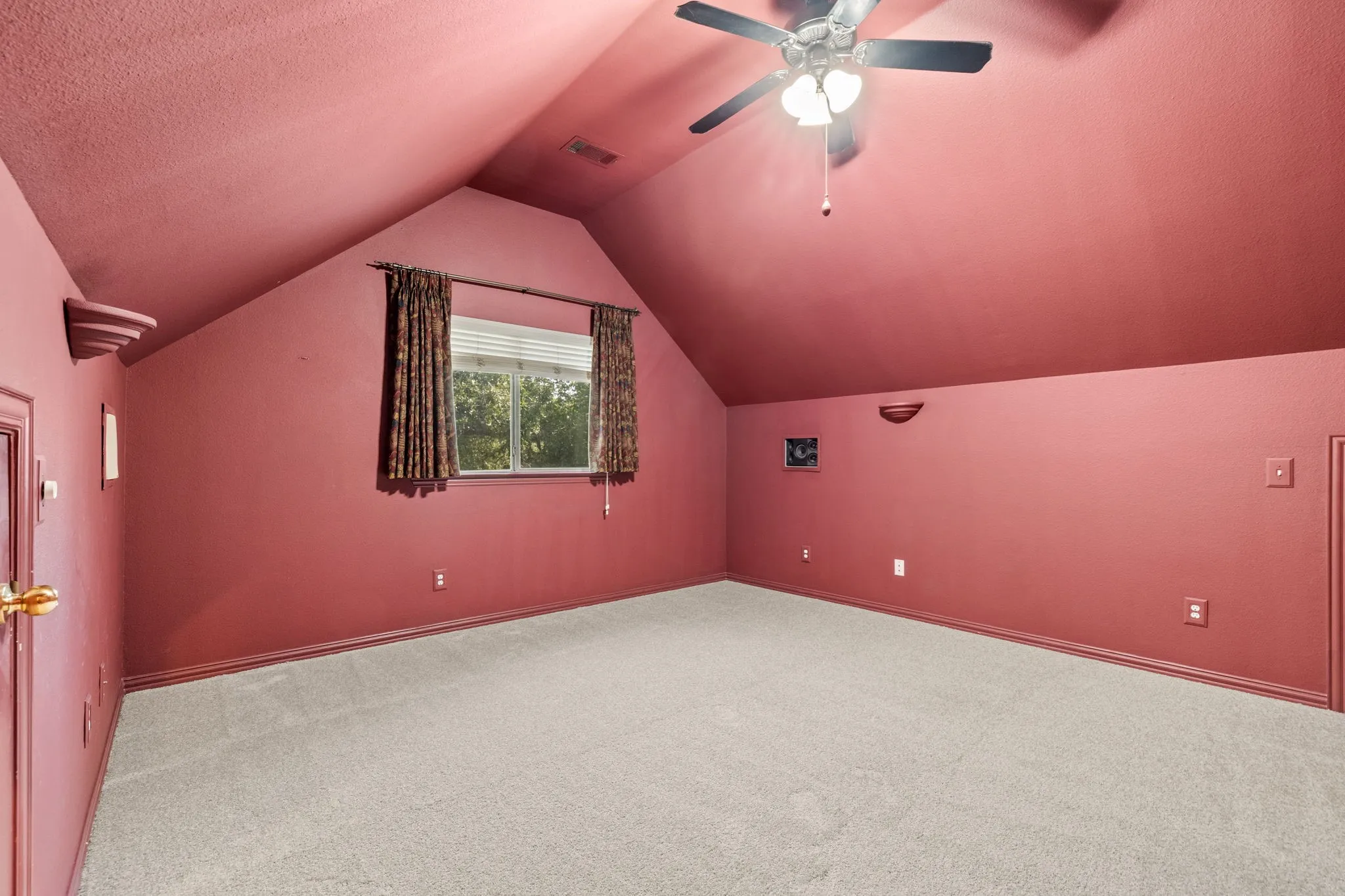Carpeted room featuring an angled ceiling, a centered window with blinds, and a ceiling fan
