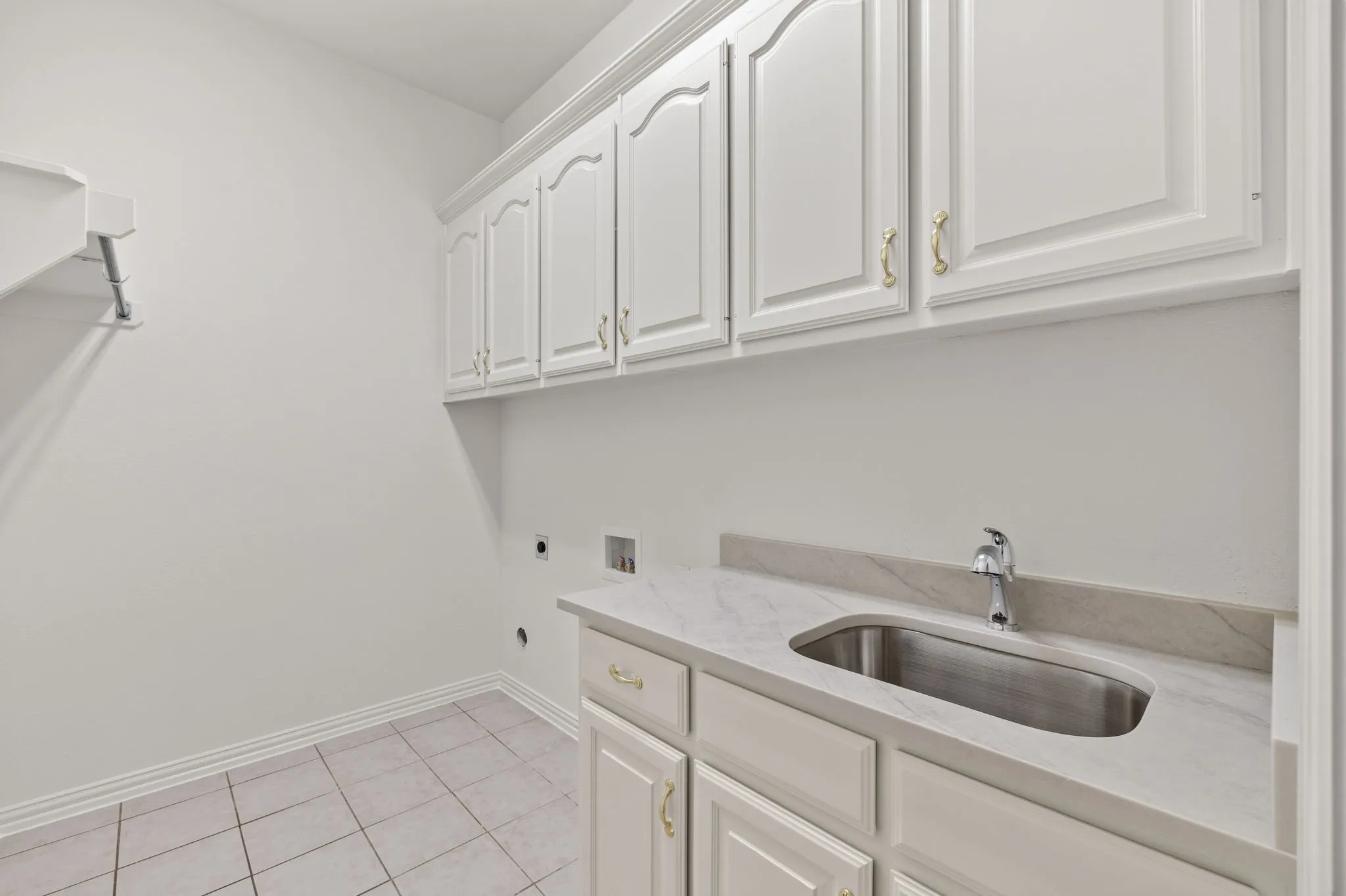 Utility room featuring white cabinetry with gold-tone hardware, a light-toned countertop, and an undermount stainless steel sink with a chrome faucet