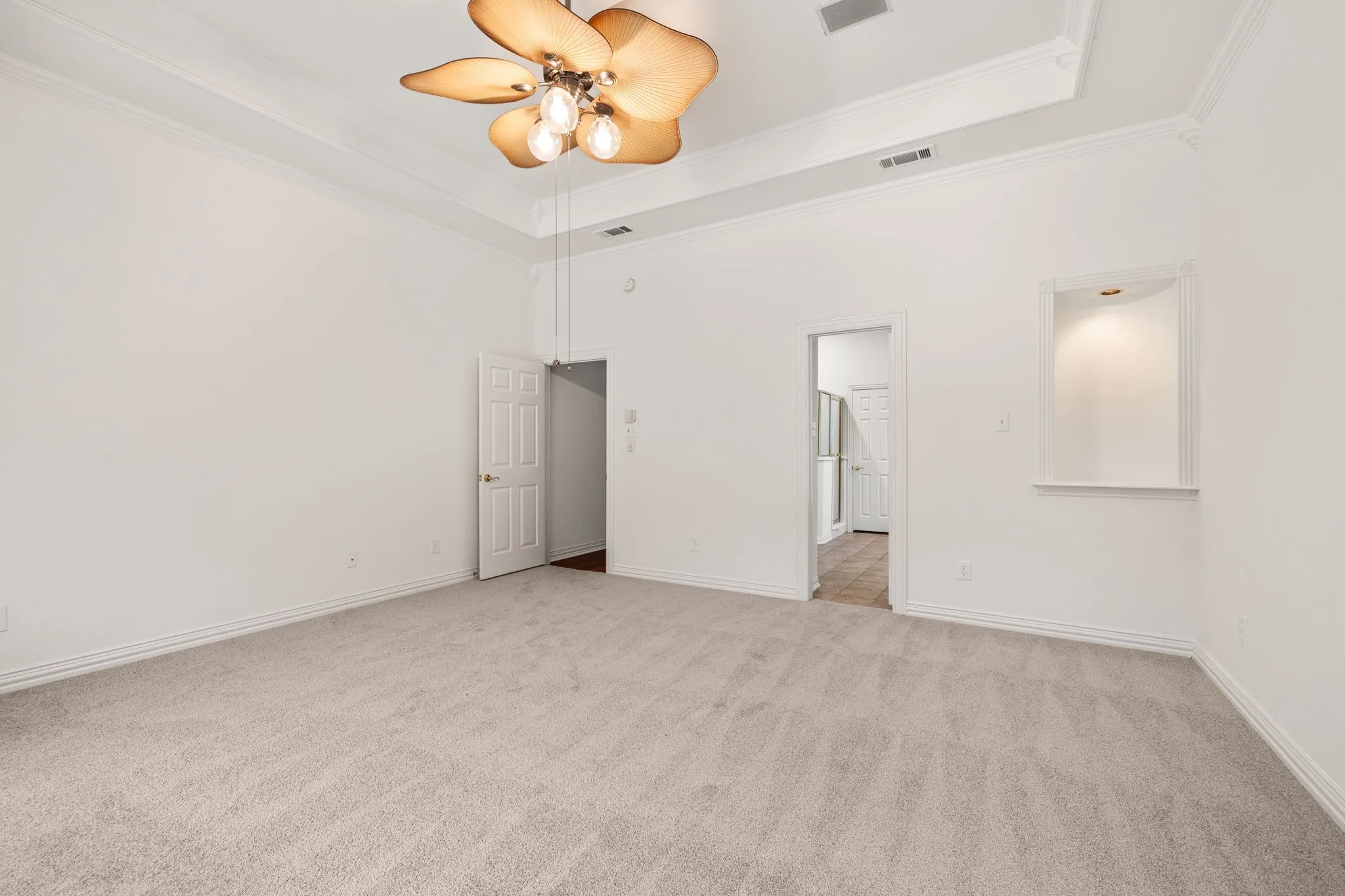 Carpeted room featuring a ceiling fan with decorative blades, tray ceiling, crown molding, and an illuminated wall niche