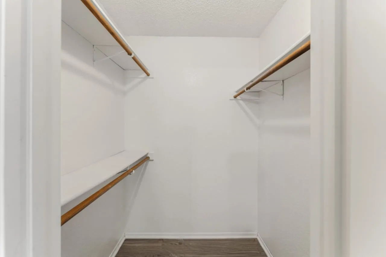 Walk-in closet with wood-finish flooring, white walls, and built-in shelving with hanging rods