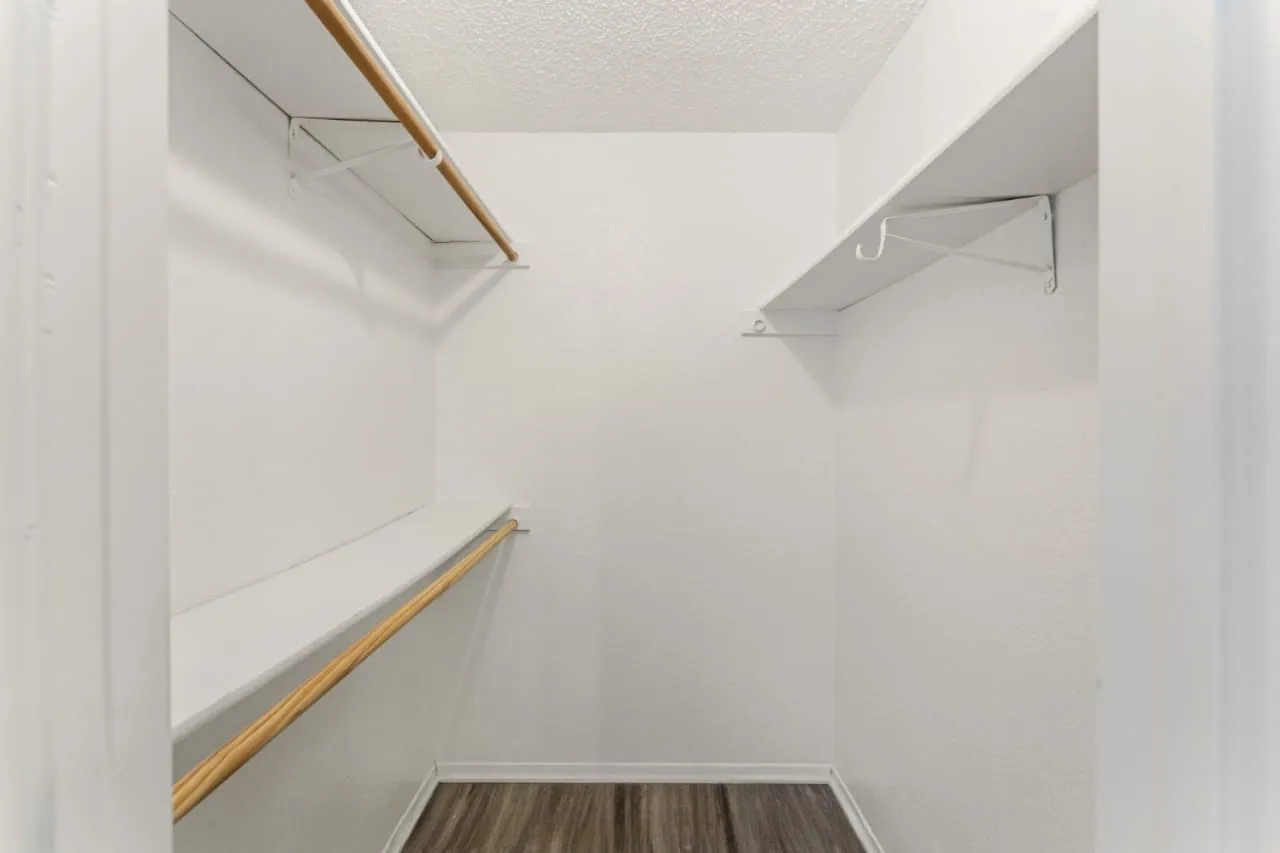 Walk-in closet featuring wood-finish flooring, white walls, and built-in shelving with hanging rods