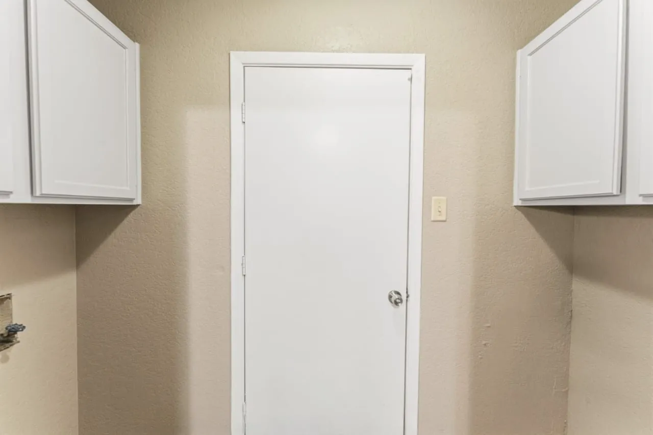 White shaker-style upper cabinetry flanks a central white door with a polished chrome doorknob, set against neutral textured walls