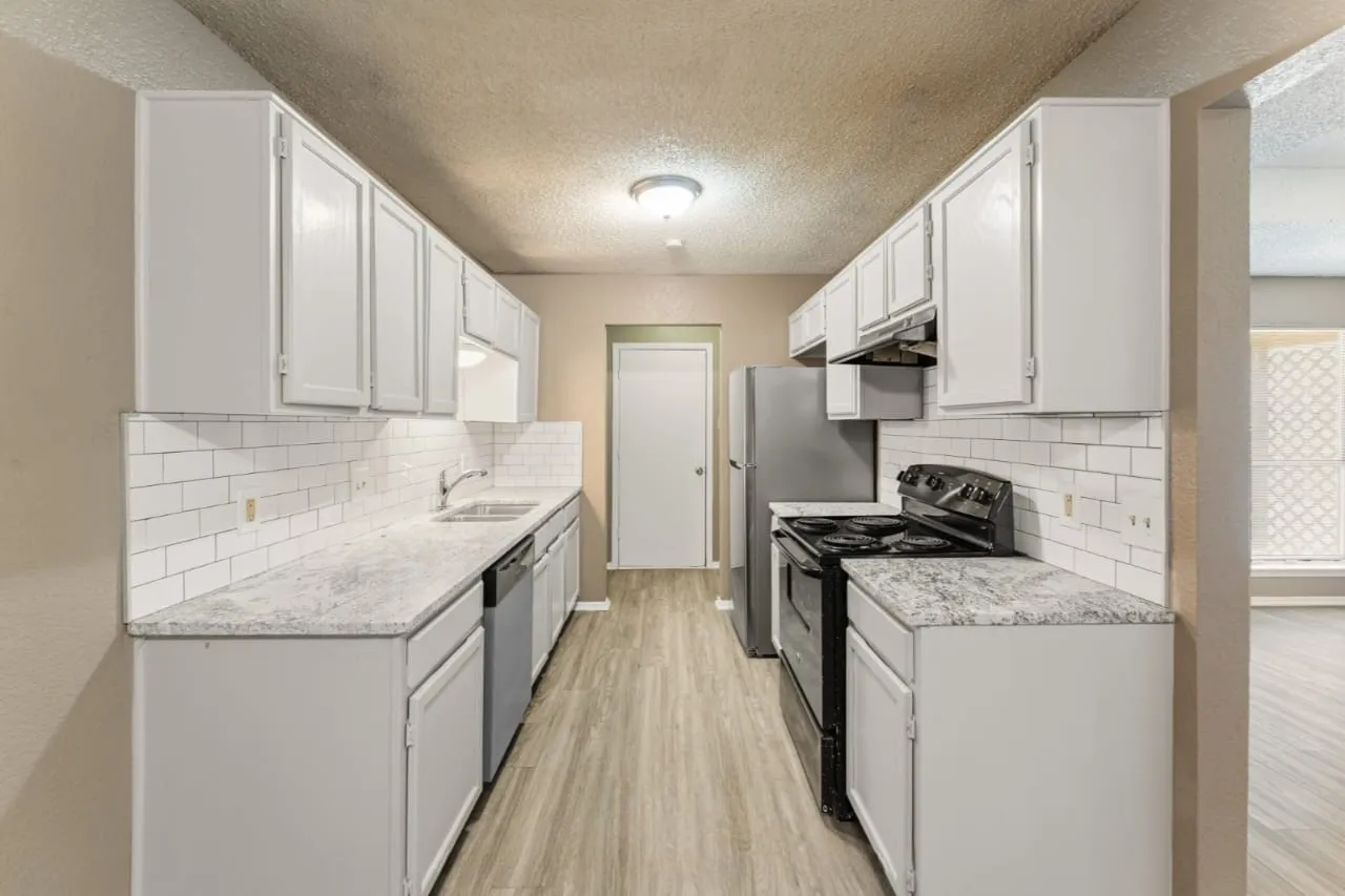 Streamlined kitchen featuring white cabinetry, light-toned wood-finish flooring, white subway tile backsplash, and speckled countertops