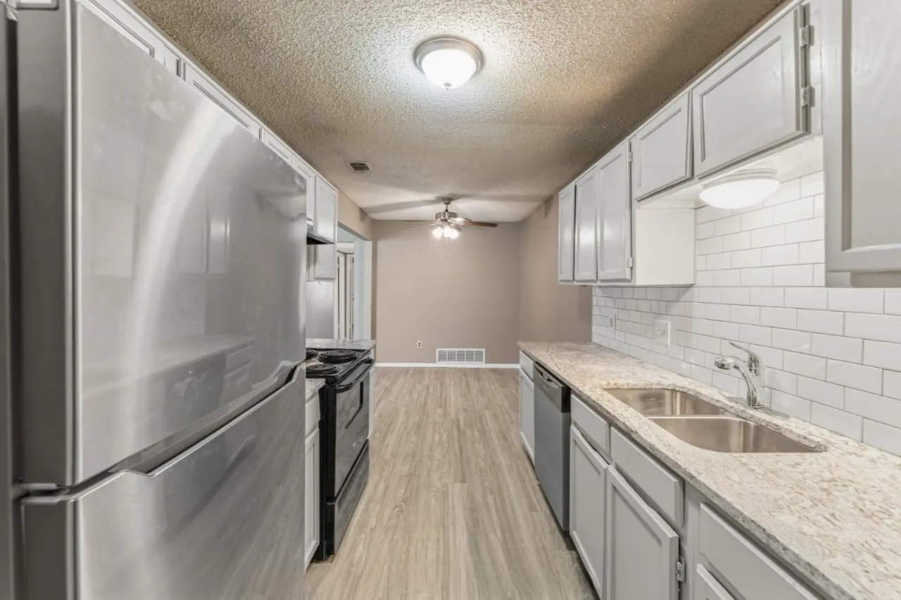 Galley kitchen featuring stainless steel appliances, light gray cabinetry, light granite-style countertops, white subway tile backsplash, and wood-finish flooring