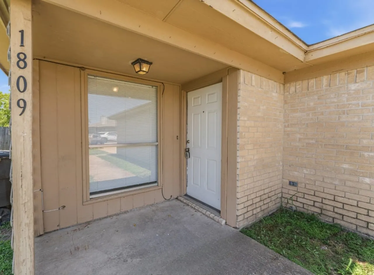 Inviting entry featuring a covered porch, brick facade, and a paneled front door