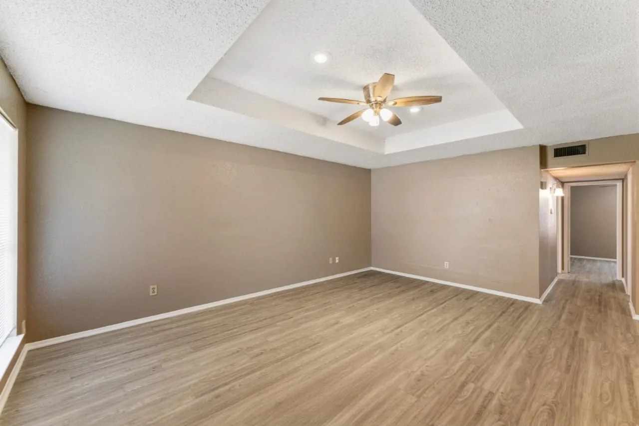 Expansive room featuring wood-finish flooring, a tray ceiling with recessed lighting, and a ceiling fan