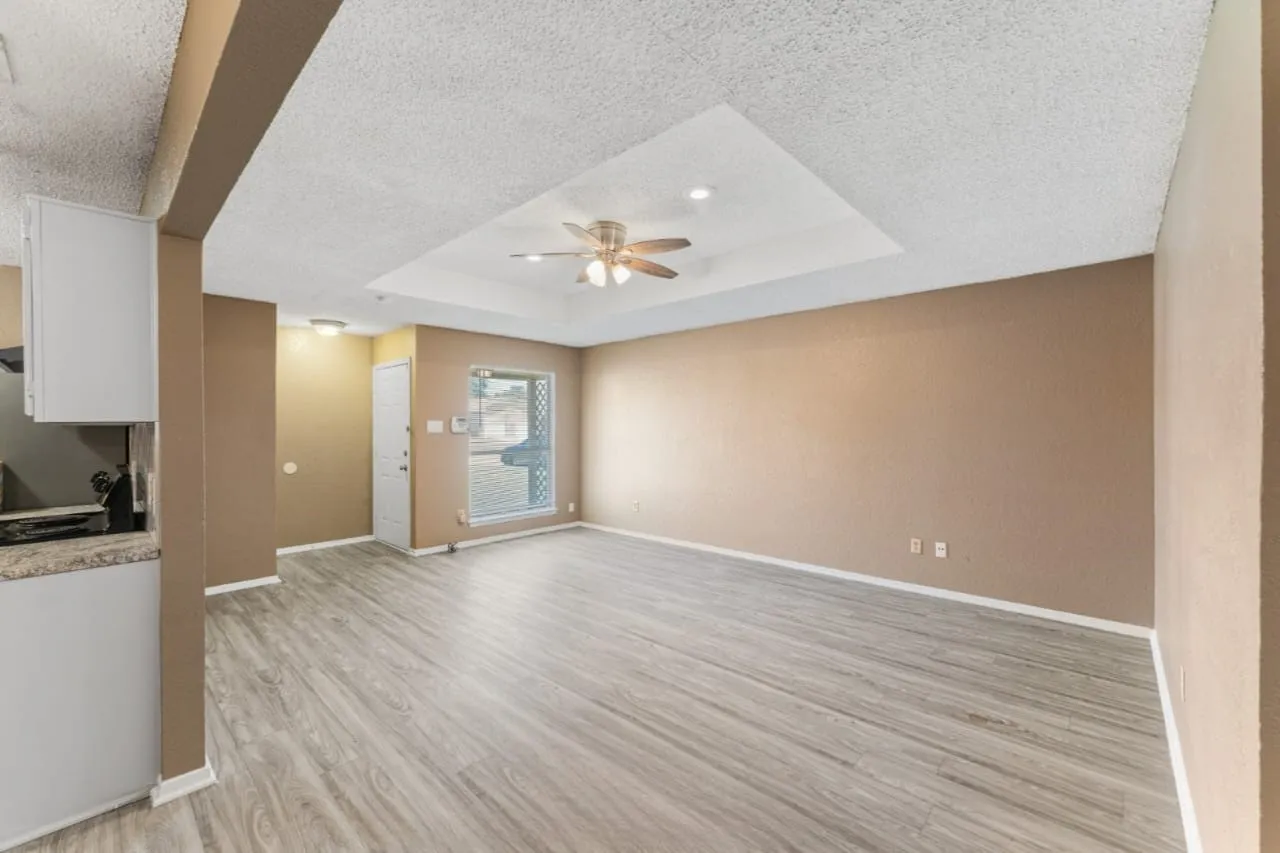Spacious room featuring light wood-finish flooring, a tray ceiling with recessed lighting, and a ceiling fan