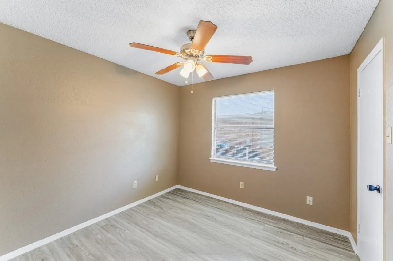 Room featuring wood-finish flooring, a ceiling fan with light kit, and a window with white trim