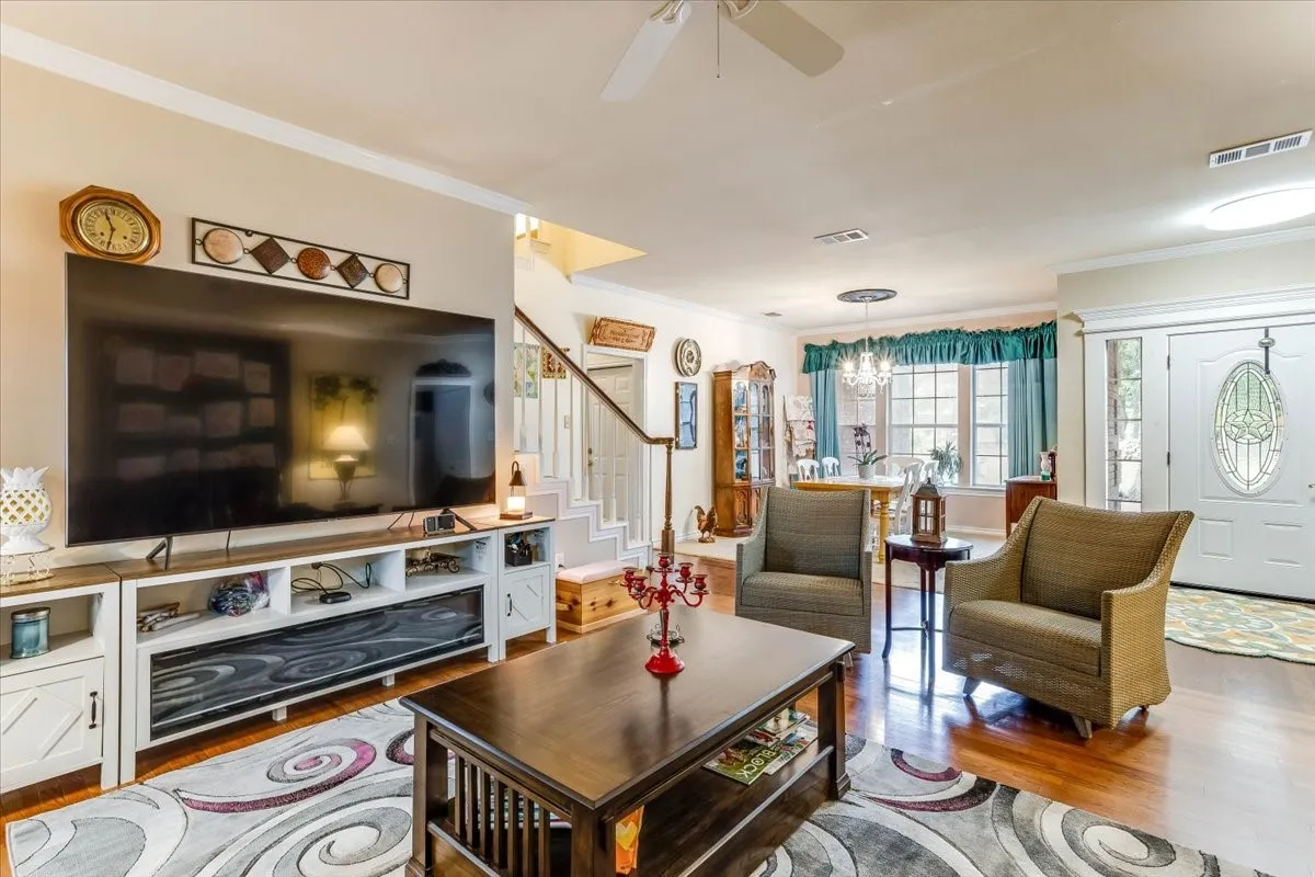 Open concept living space featuring wood-finish flooring, crown molding, and a visible staircase with white risers