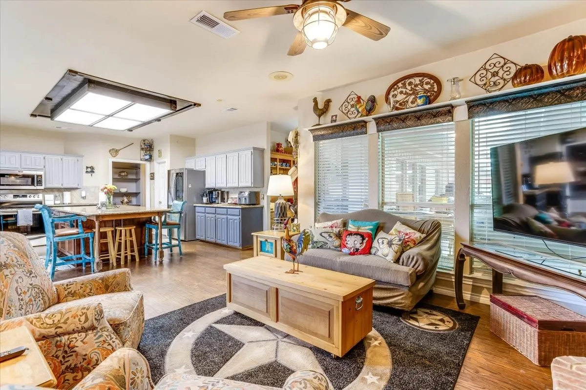 Open-concept living area with wood-finish flooring, a ceiling fan, and multiple windows