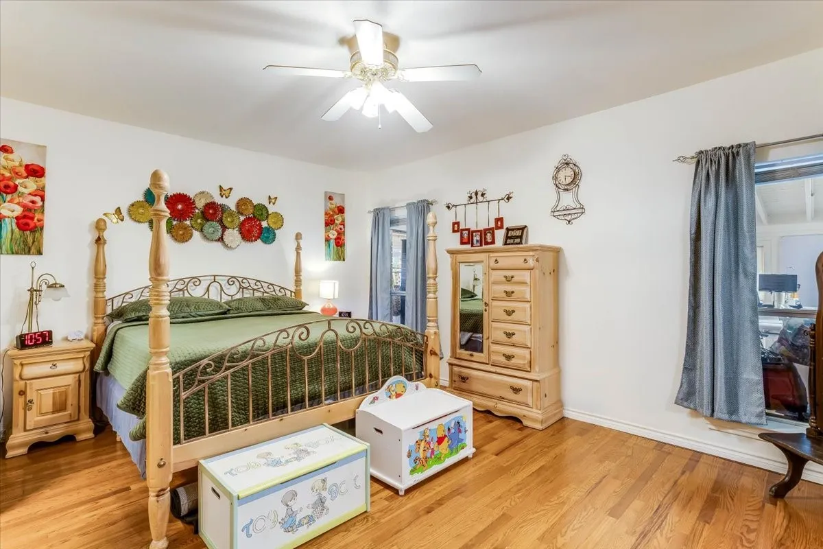 Bright room featuring wood-finish flooring, a ceiling fan with integrated lighting, and multiple windows with curtain rods