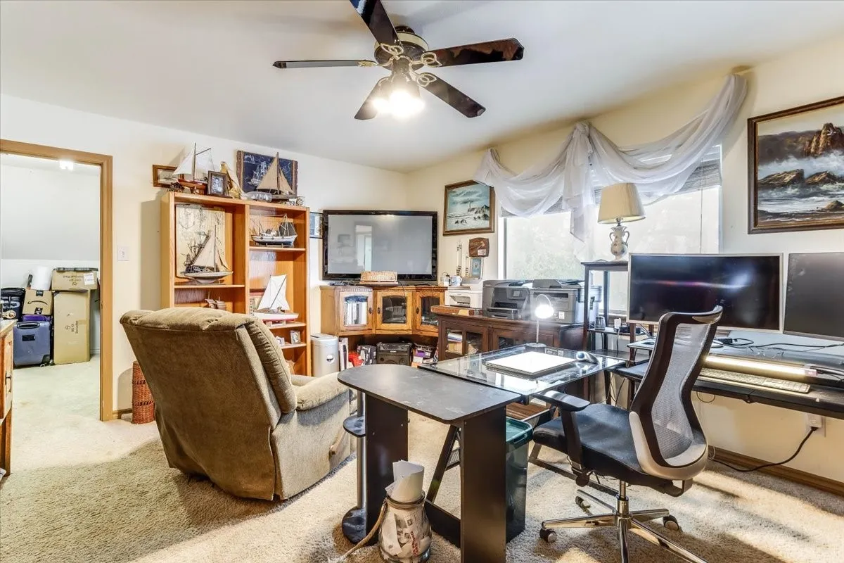 Home office space featuring light-toned carpeting, a ceiling fan with integrated lighting, and a large window