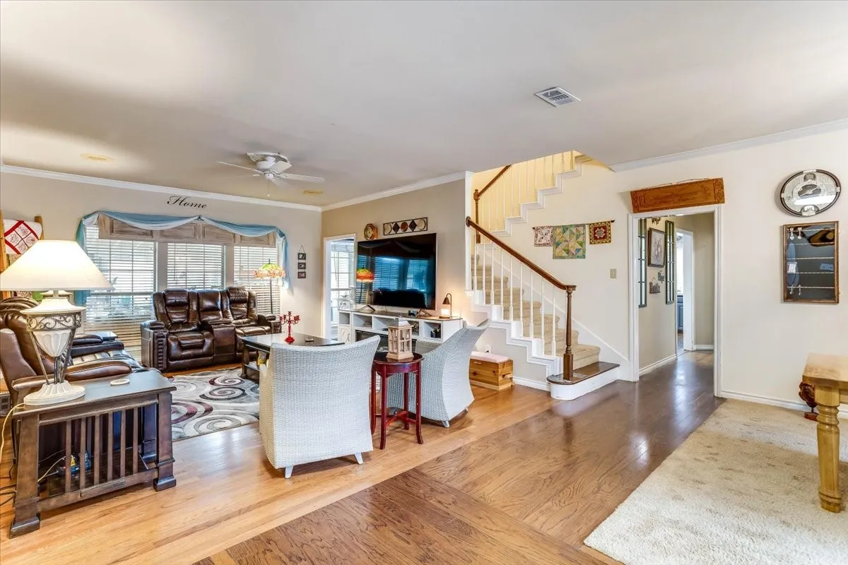 Spacious living area featuring polished wood-finish flooring, a prominent staircase with wood banister, and a ceiling fan
