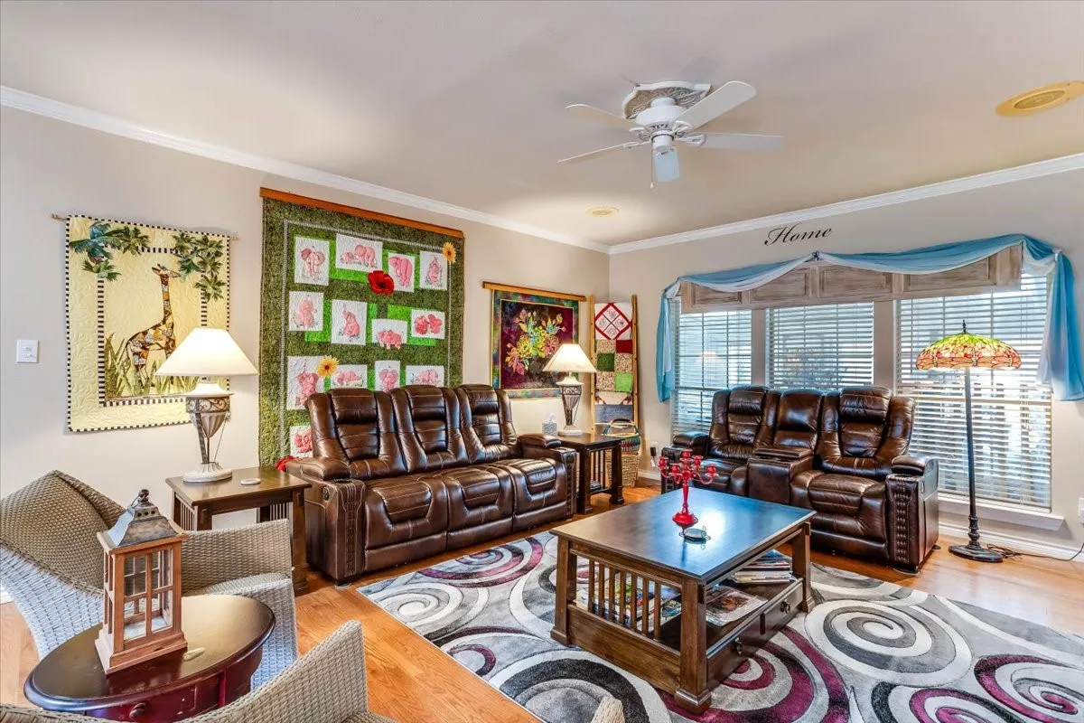 Spacious living area featuring wood-finish flooring, a ceiling fan, and large windows with horizontal blinds