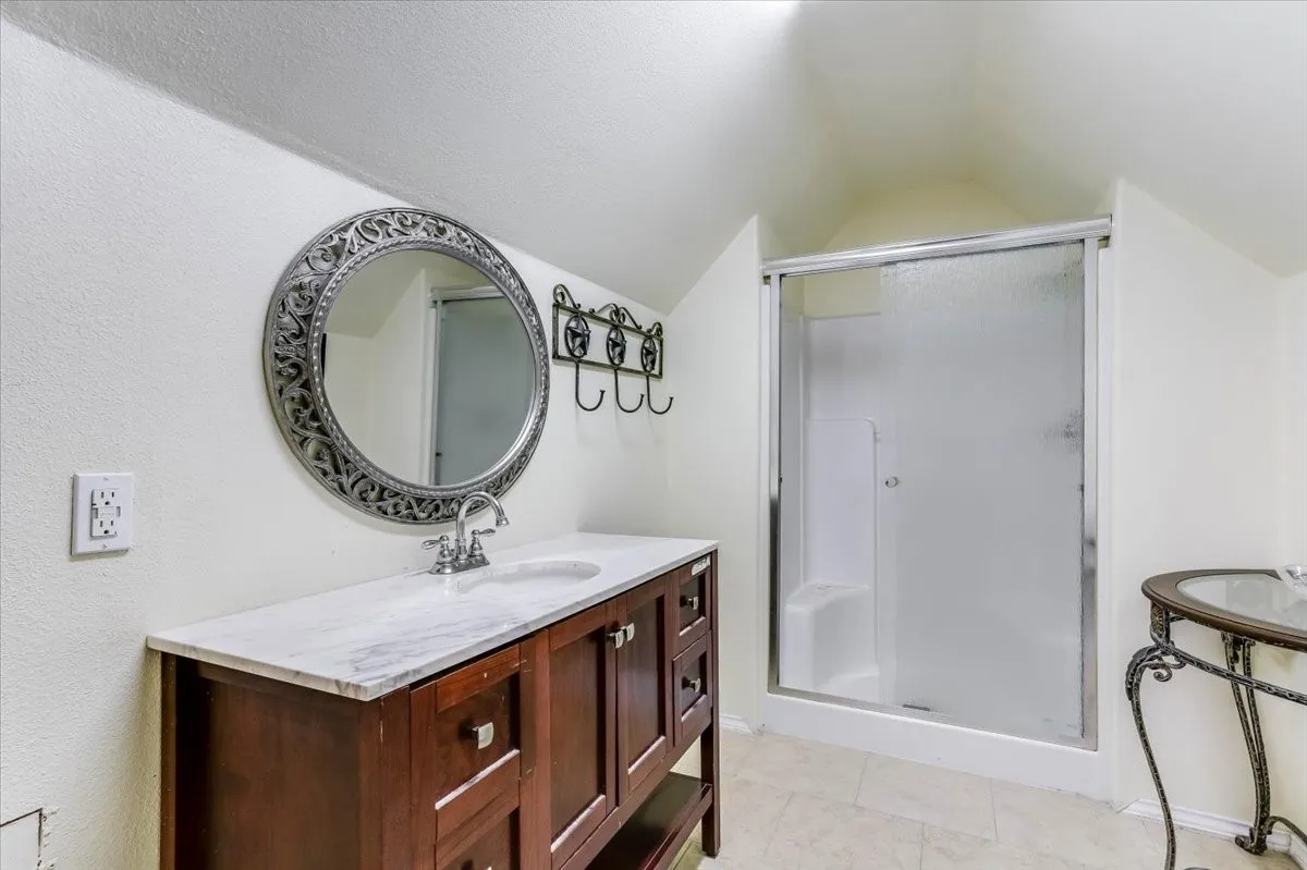 Bathroom featuring a wood-finish vanity with a light-colored countertop, an undermount sink, and a framed circular mirror