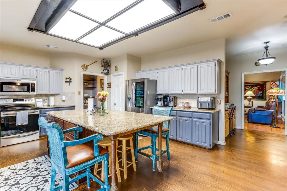 Kitchen featuring a large skylight, an expansive island with a granite countertop, stainless steel appliances, and wood-finish flooring