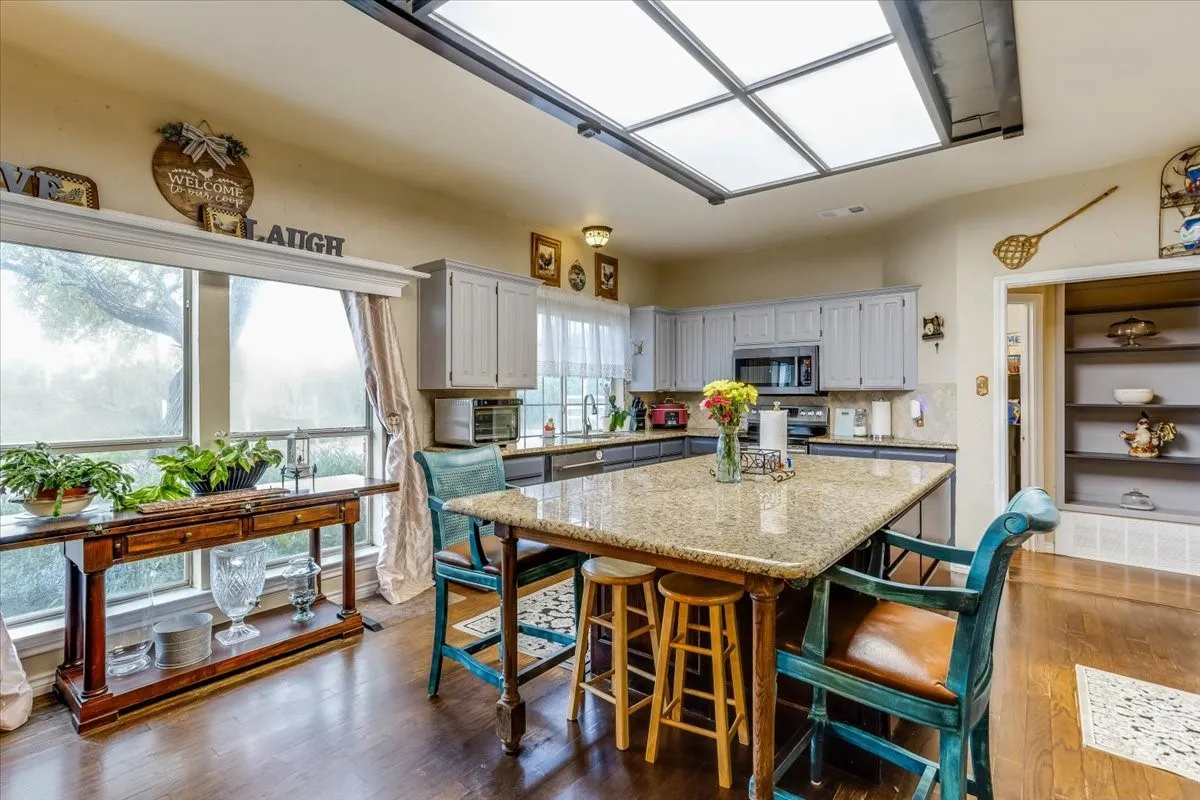 Kitchen featuring a large central island with a stone-finish countertop, wood-finish flooring, a skylight, light-toned cabinetry, and built-in shelving