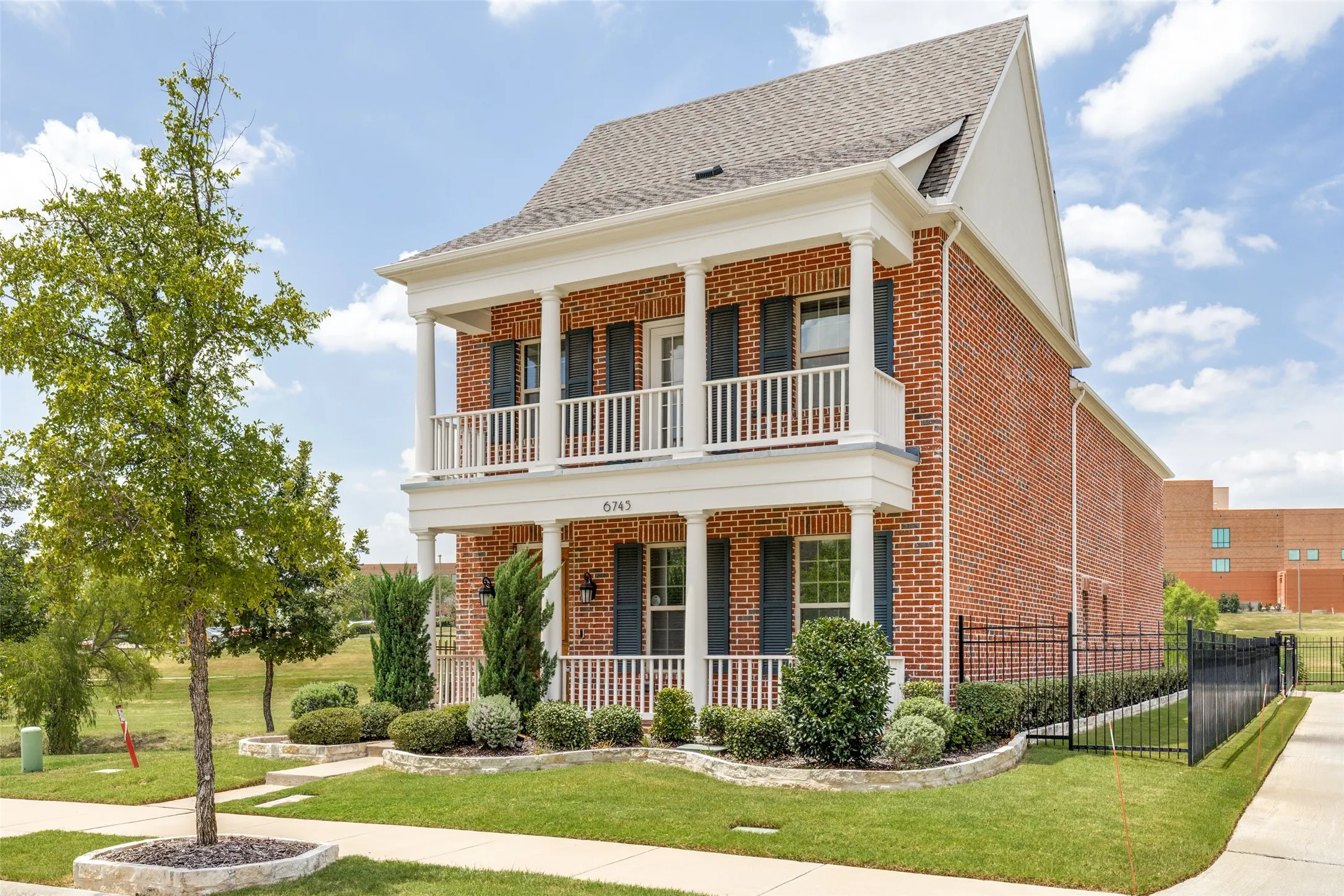 Two-story brick exterior featuring a covered porch and upper-level balcony with white columns and railings