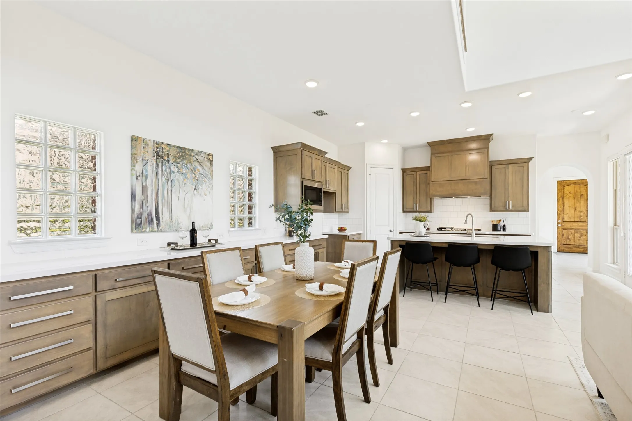 Open-concept living area featuring a kitchen with light wood-finish cabinetry, a large kitchen island with counter seating, and white subway tile backsplash