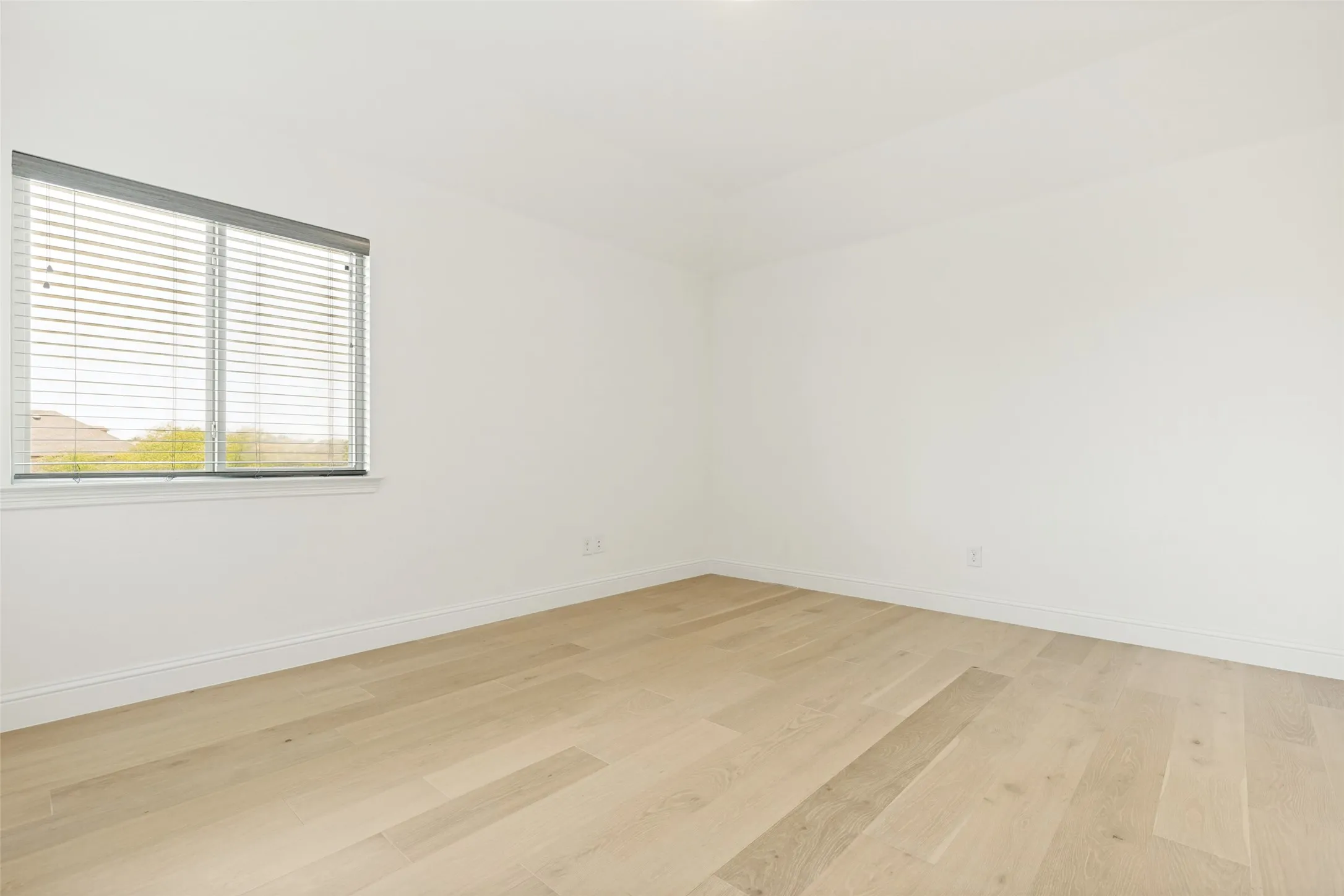 Light-toned wood-finish flooring with white baseboards and walls