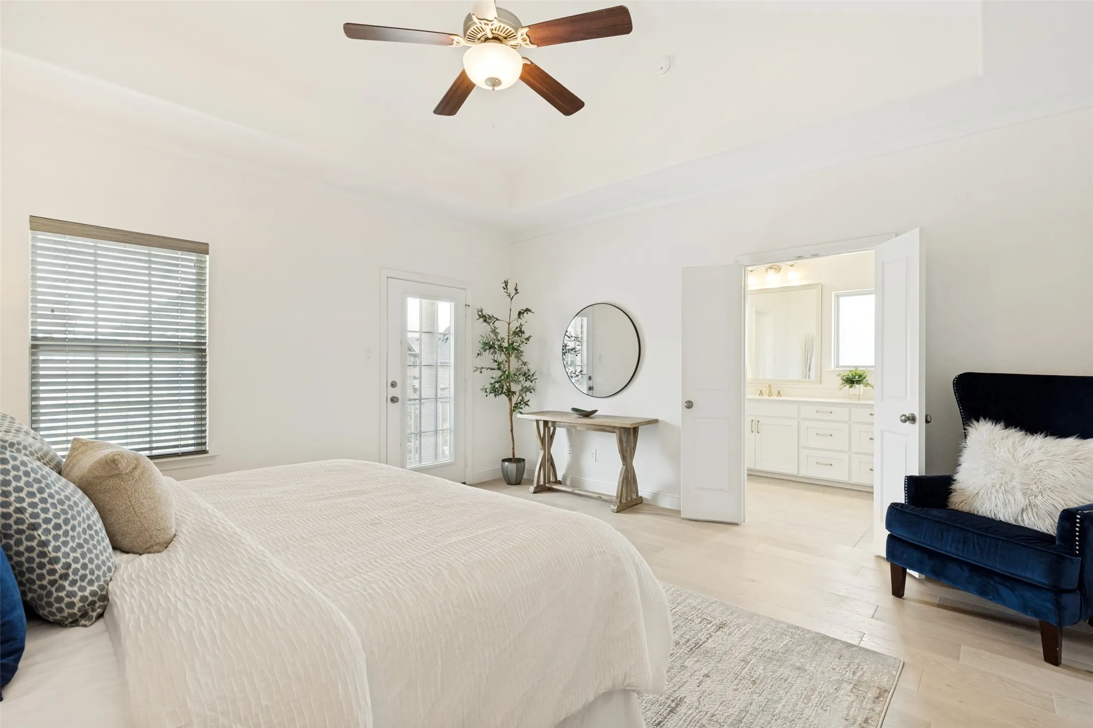 Spacious bedroom featuring light wood-finish flooring, a tray ceiling, and a ceiling fan with integrated lighting