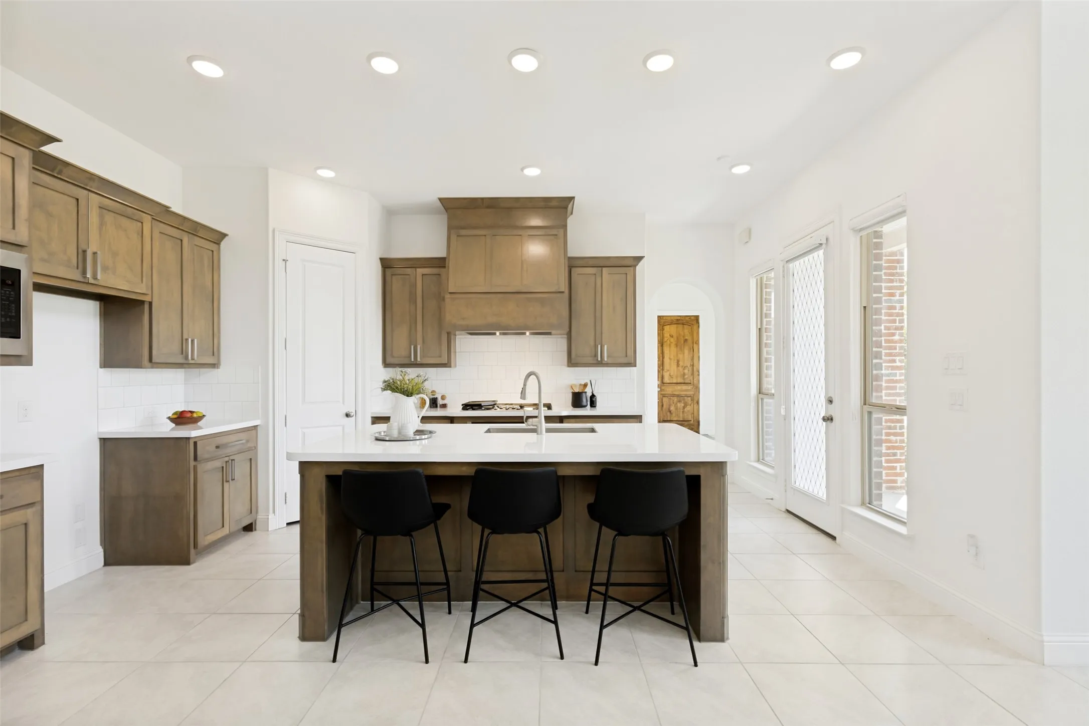 Spacious kitchen featuring an expansive center island with seating, wood-finish cabinetry, crisp white countertops, a subway tile backsplash, and recessed lighting
