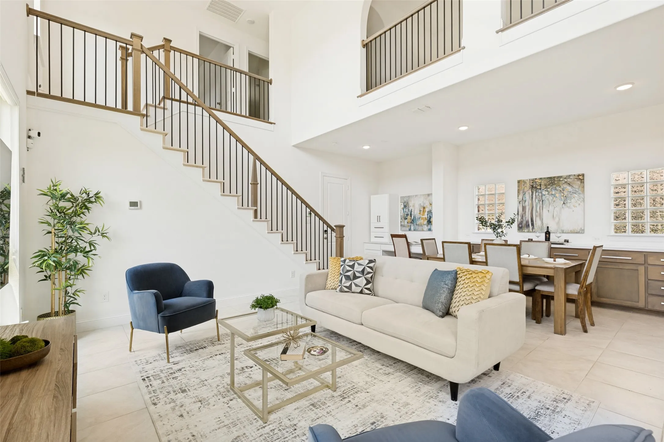 Grand two-story living area featuring a prominent staircase with wood-finish handrails and black metal balusters