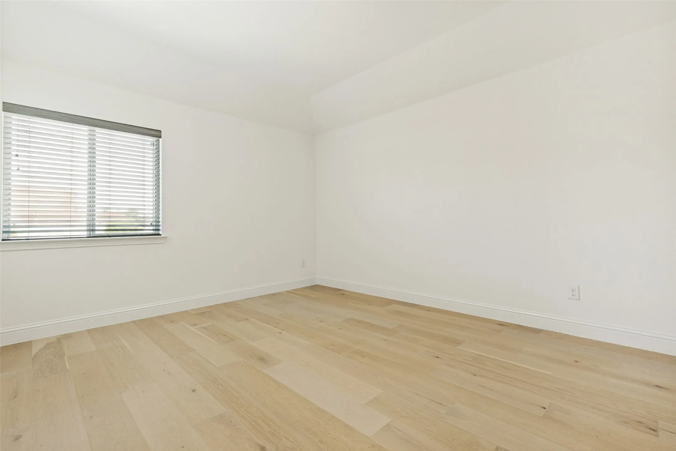 Bright interior space featuring light wood-finish flooring, white baseboards, and a window with horizontal blinds