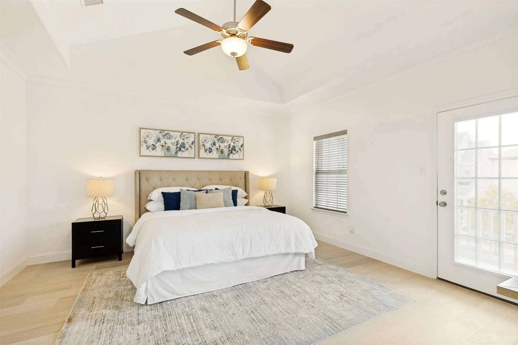 Spacious bedroom featuring light wood-finish flooring, a tray ceiling, and a ceiling fan